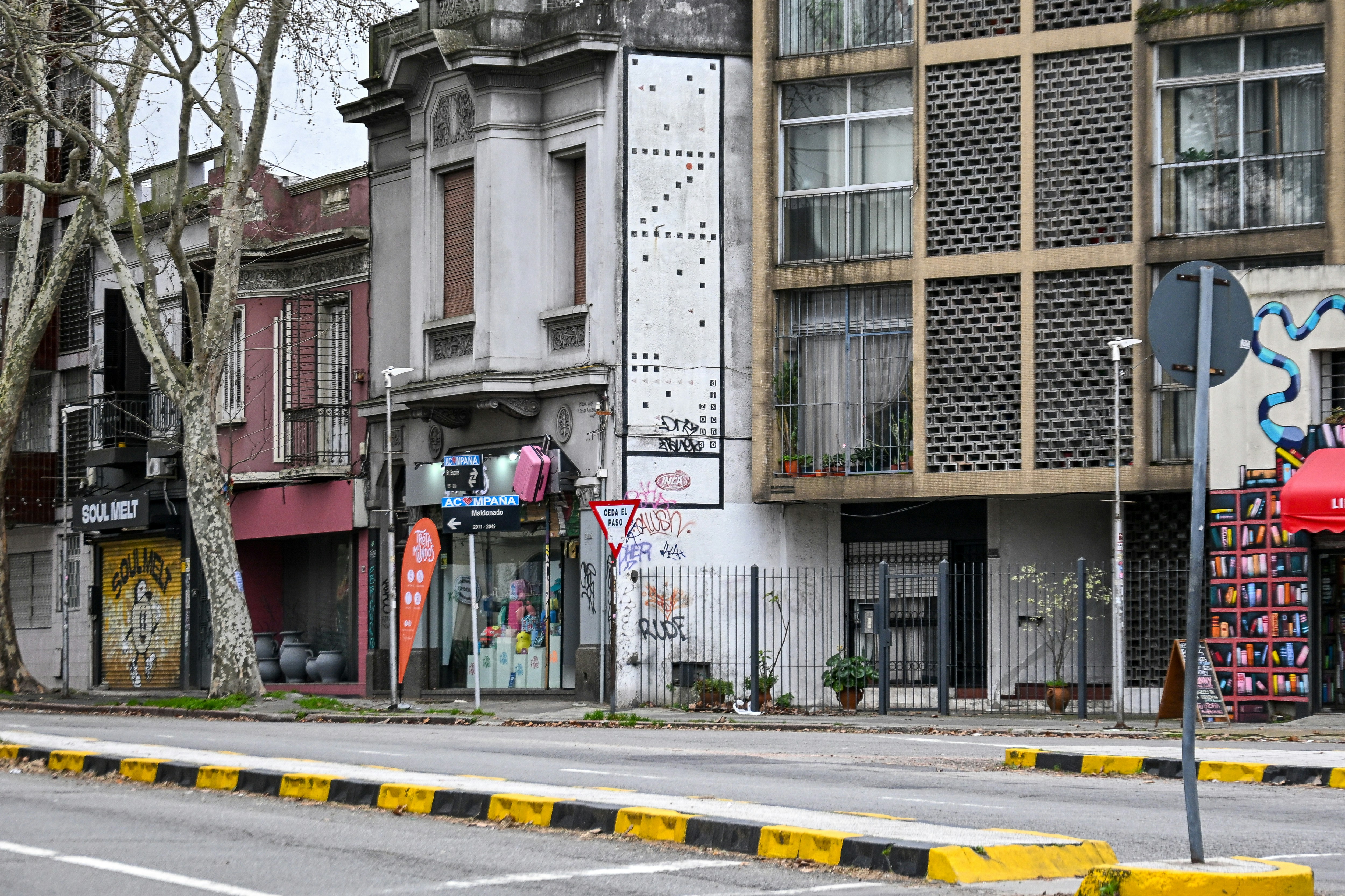 A street with storefronts and apartment buildings featuring graffiti and a large vertical mural