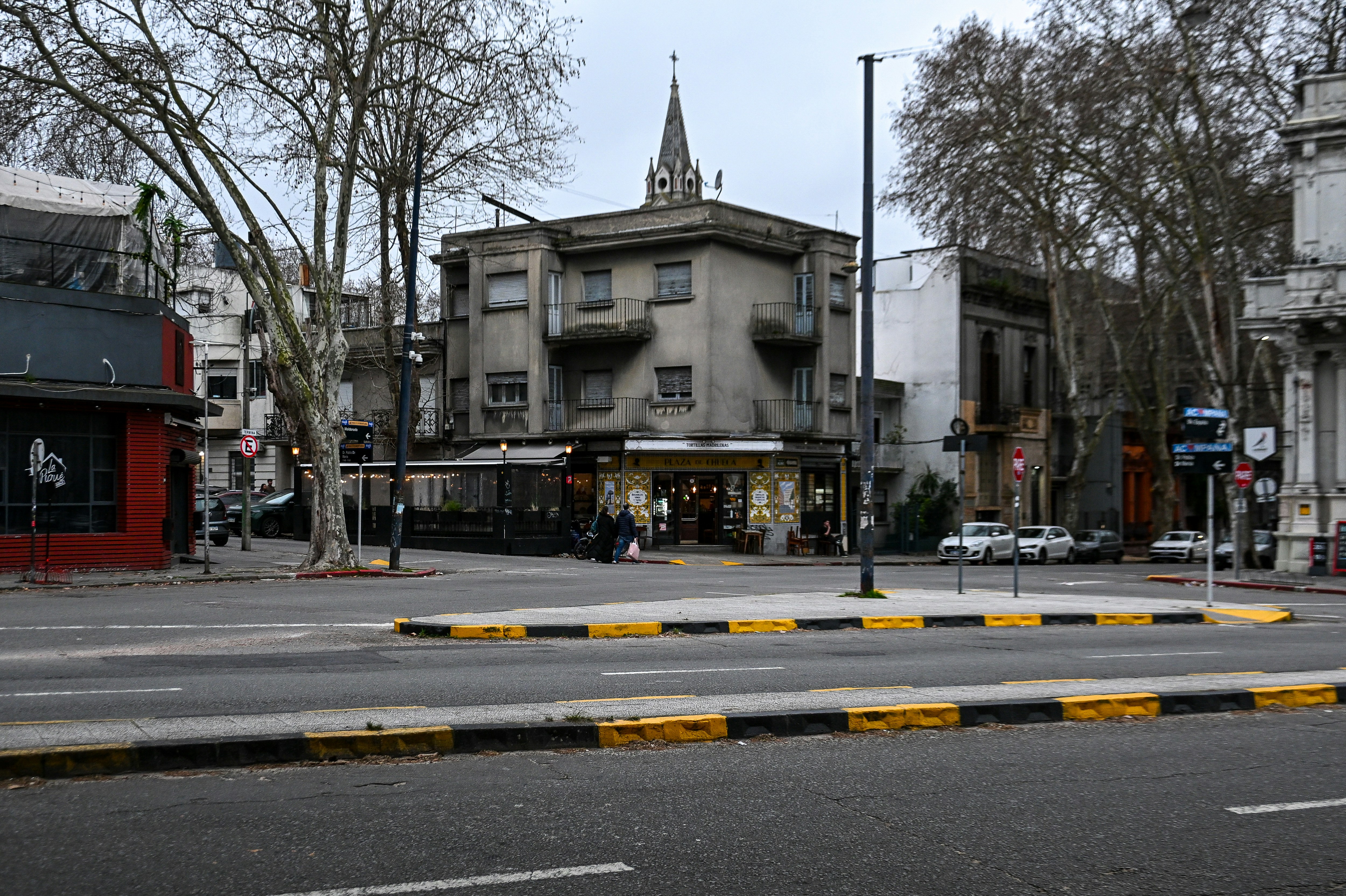 A street corner with a grey building and a small church spire