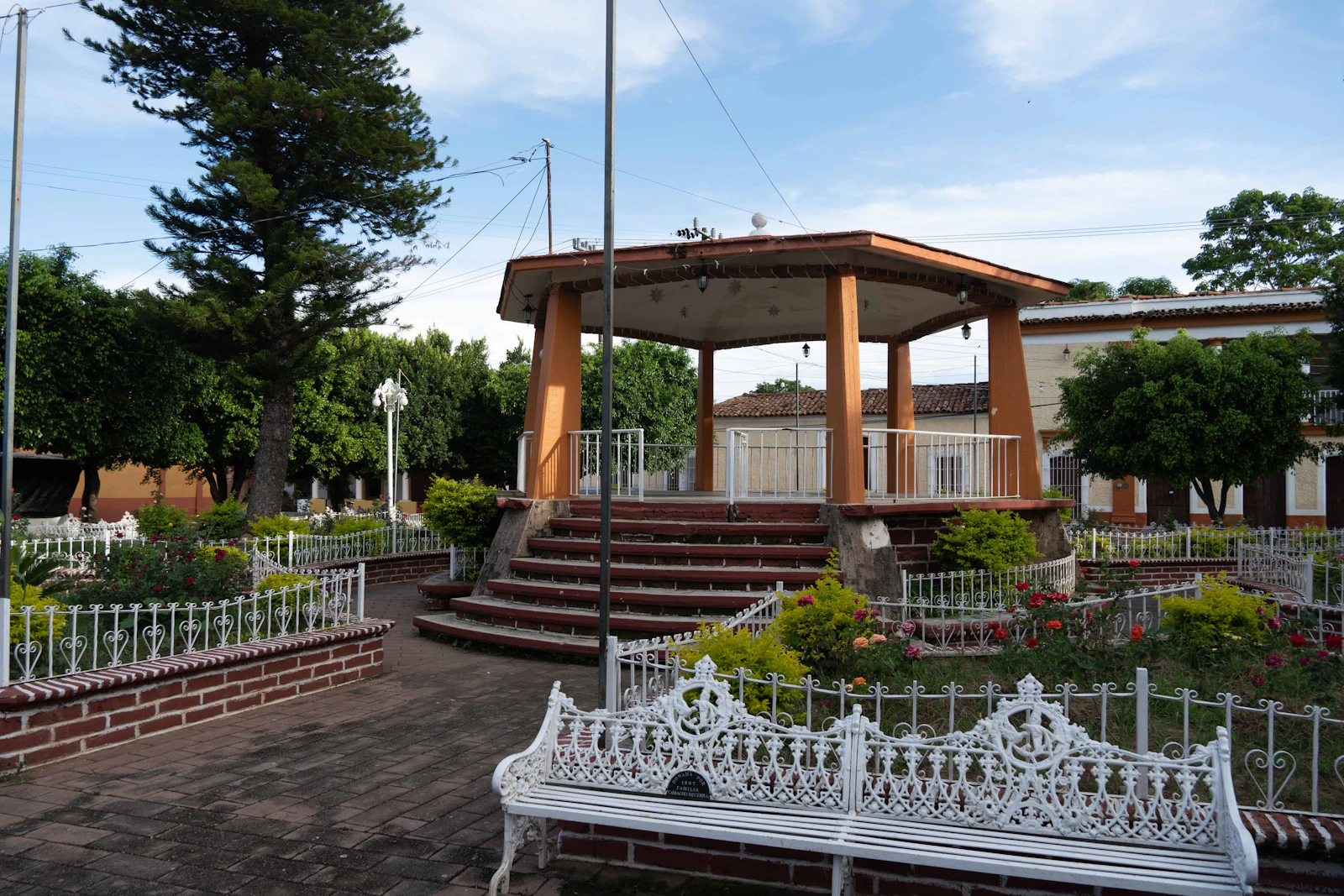 A wooden bandstand on a village green behind a white fence.