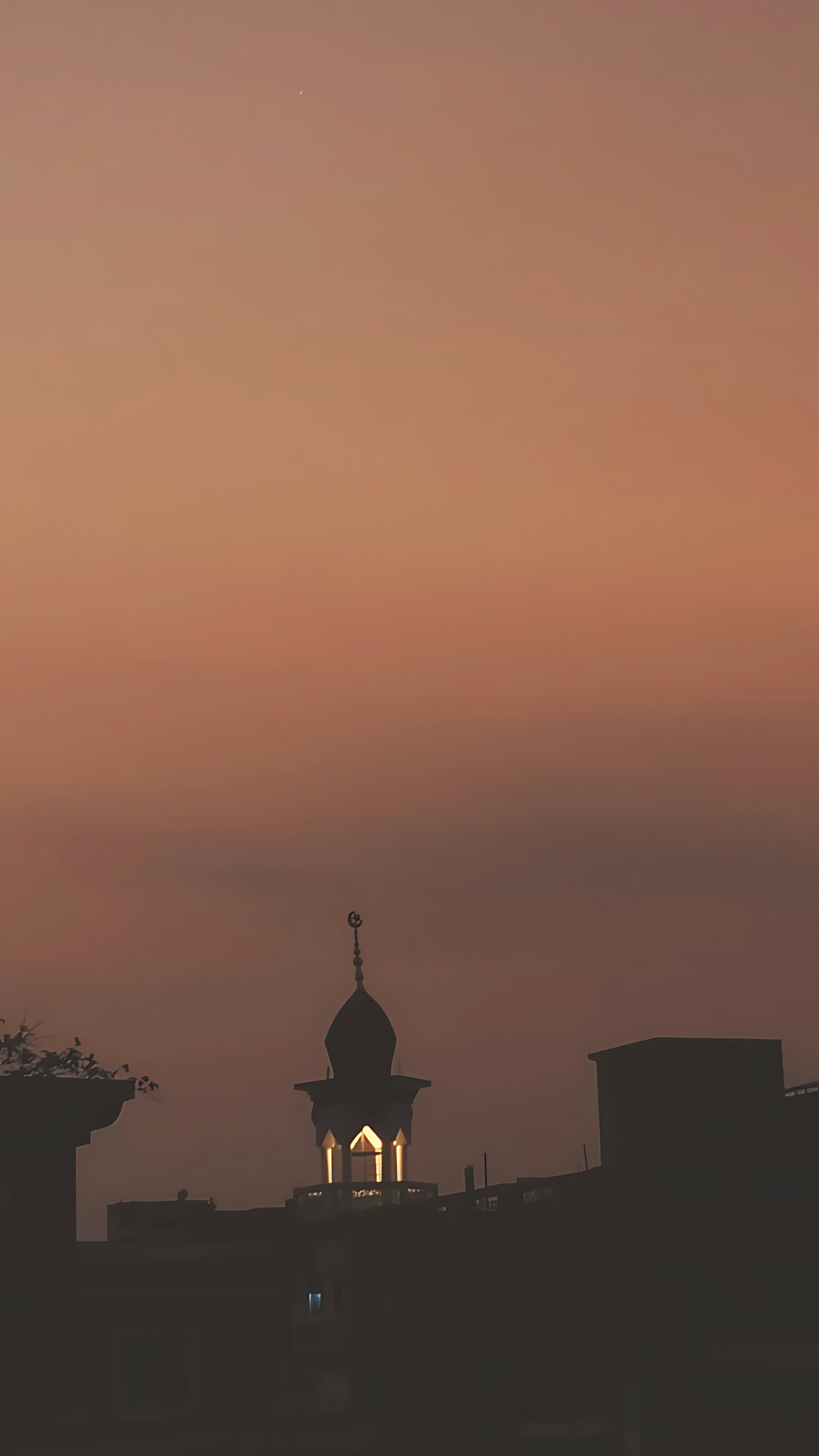A mosque minaret silhouette against a warm orange sky at low light