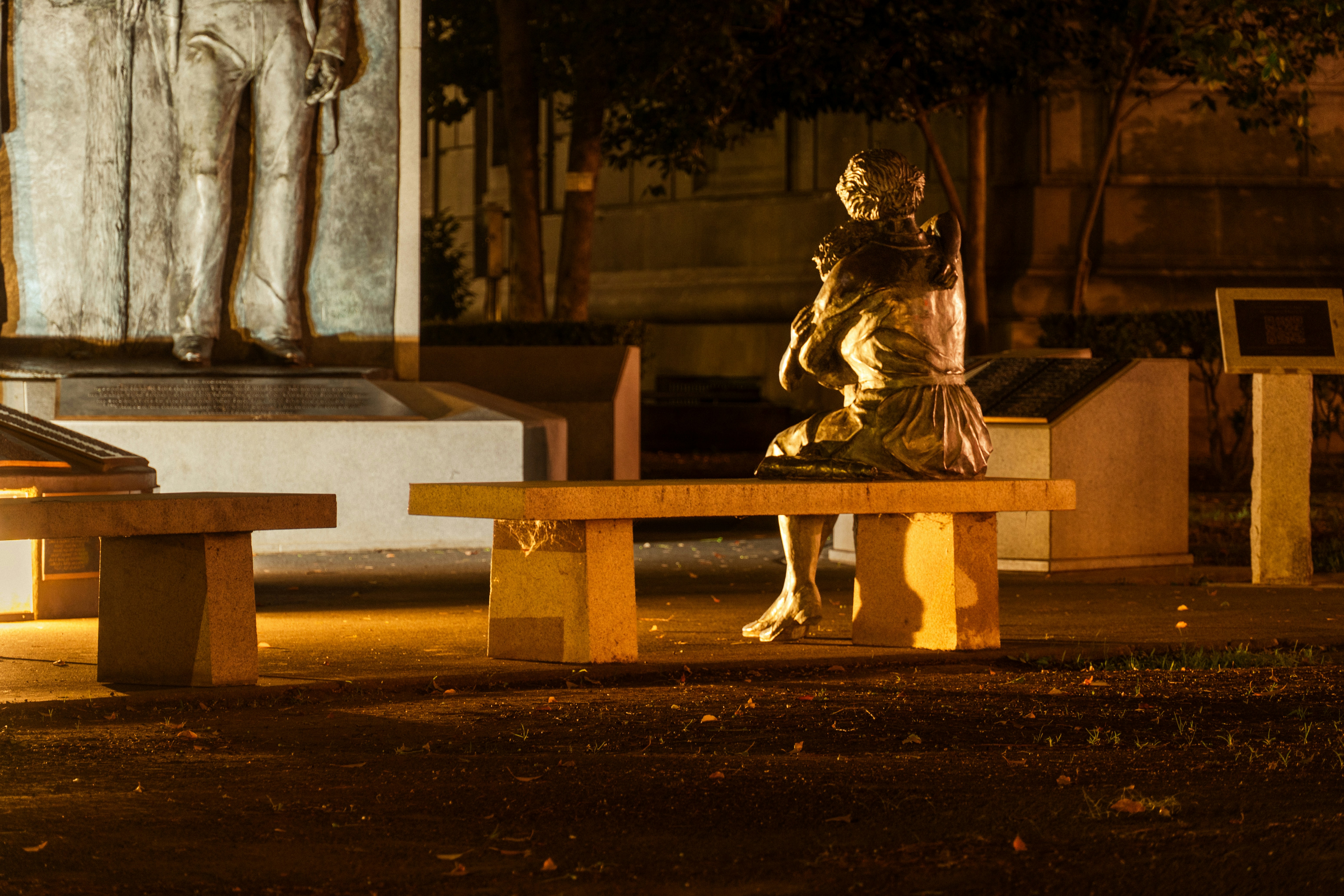 A bronze statue of a person holding a child on a stone bench