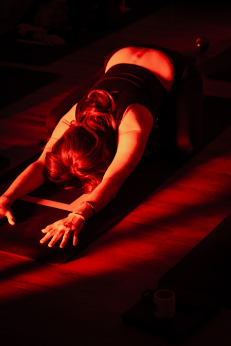 Woman resting in child's pose on a yoga mat under warm red light