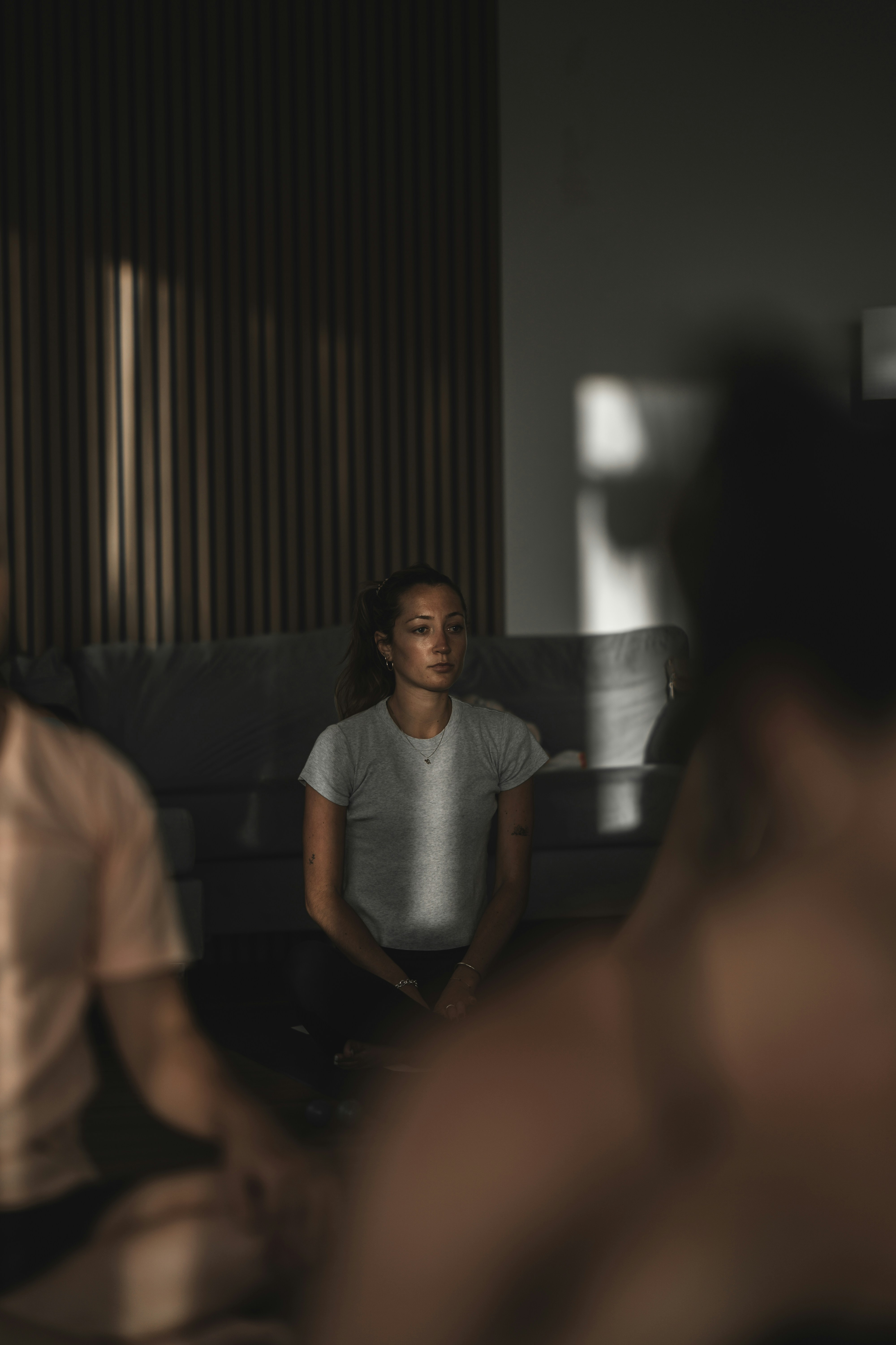 A woman in a grey t-shirt sitting on the floor in a dimly lit room