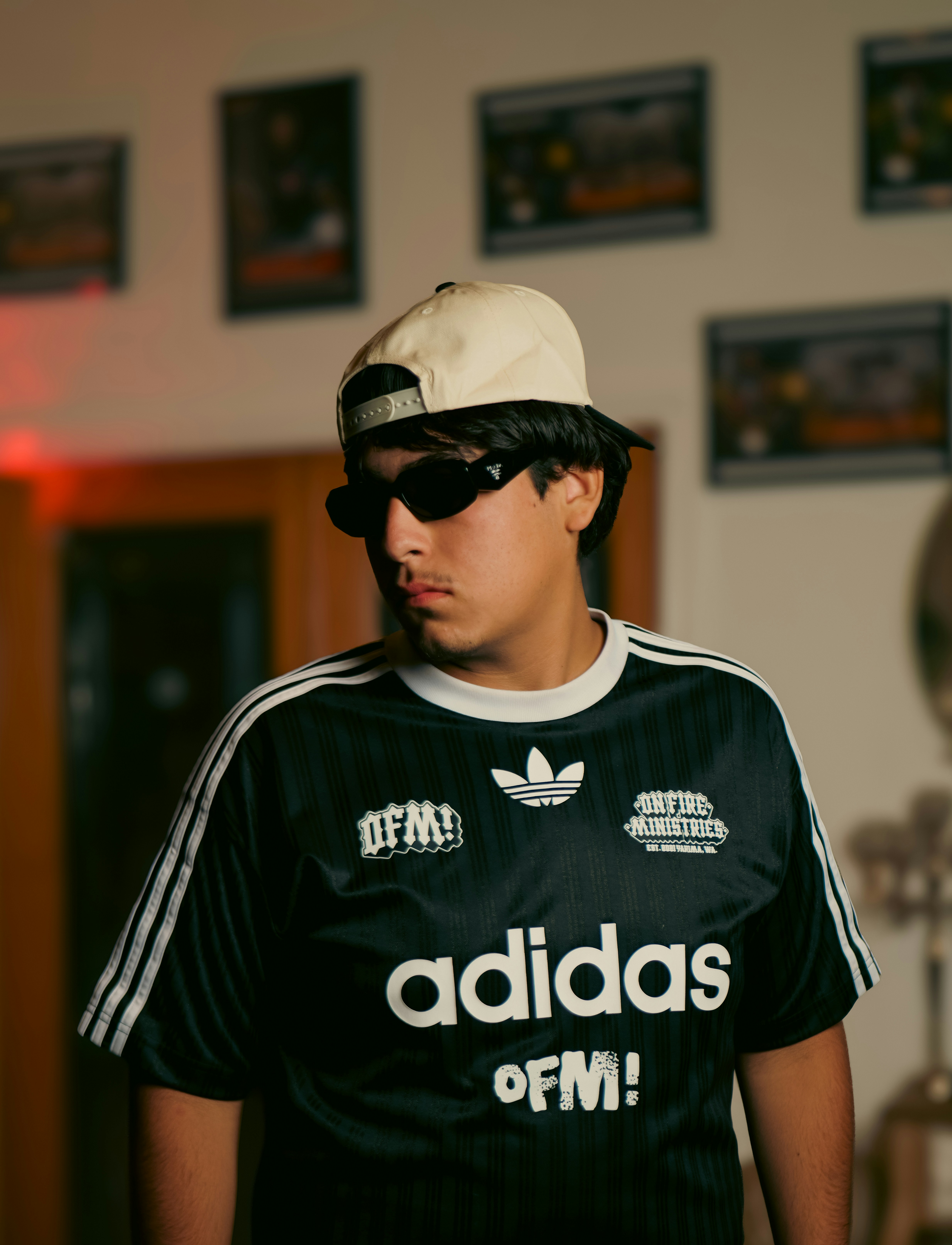 A person wearing a black jersey, sunglasses, and a beige cap indoors