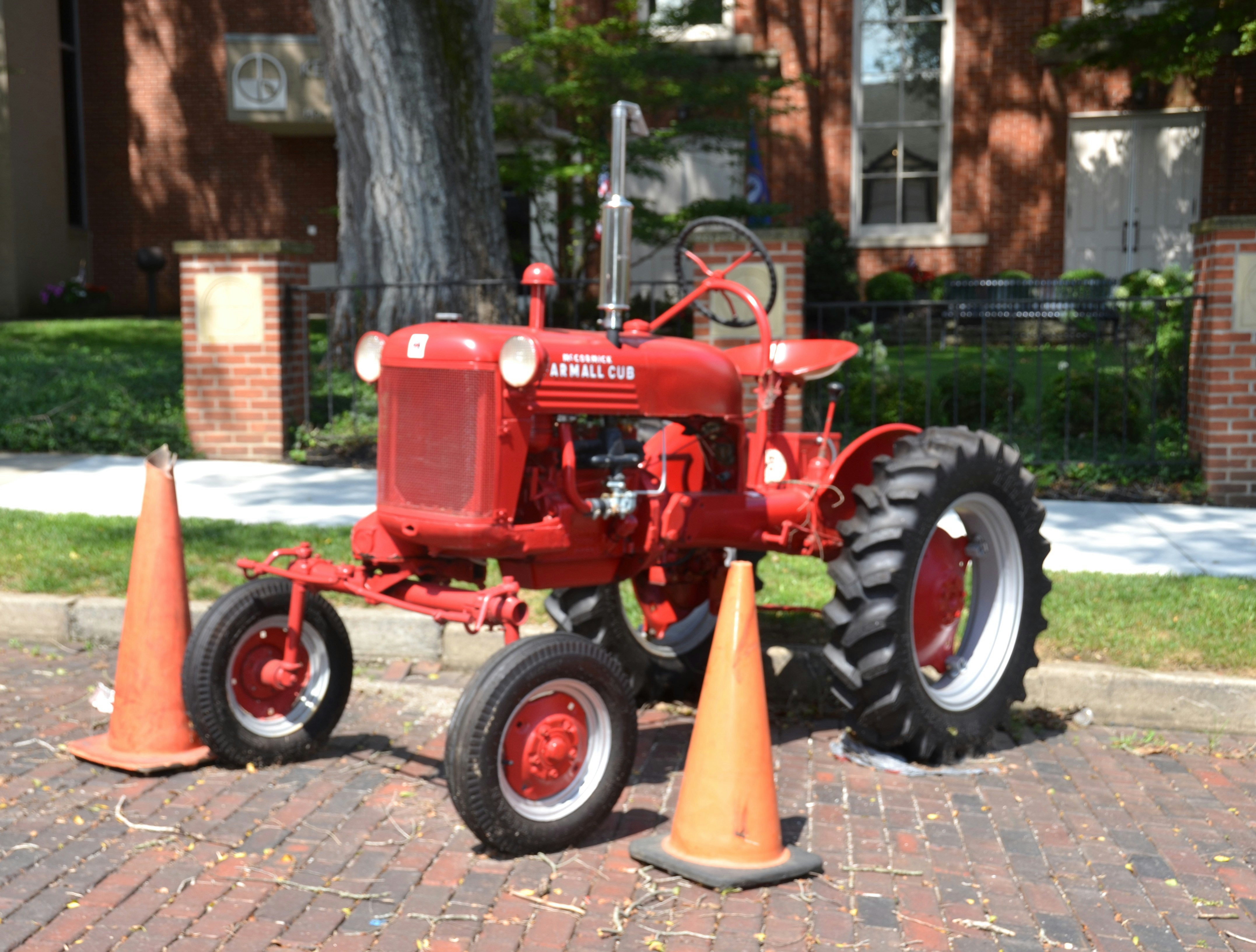 Um trator Farmall Cub vermelho vintage estacionado em uma superfície de tijolos com cones laranja
