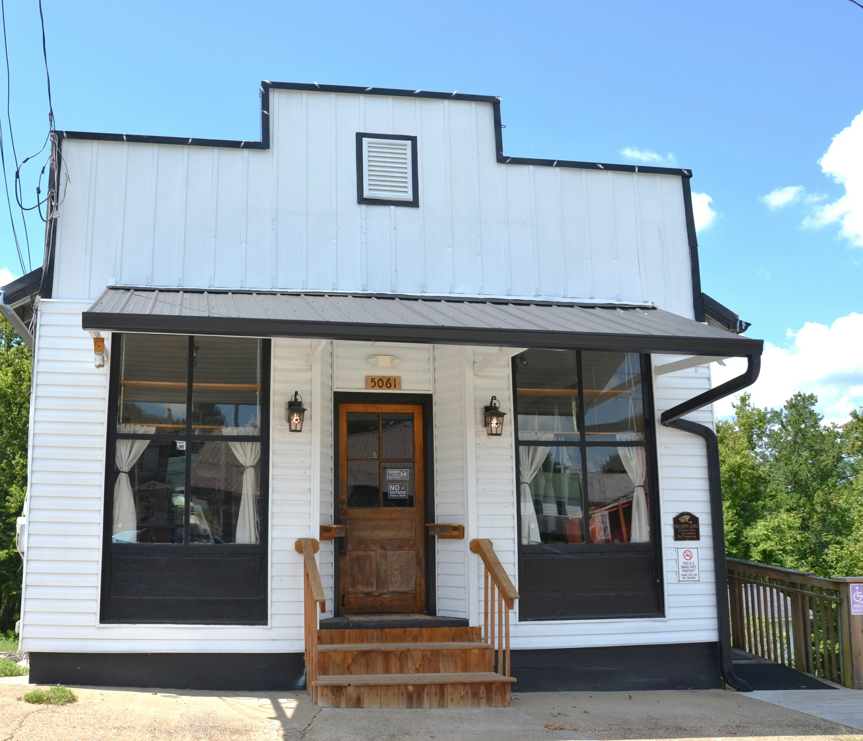 Small white commercial building with a covered porch, wood entrance door and display windows