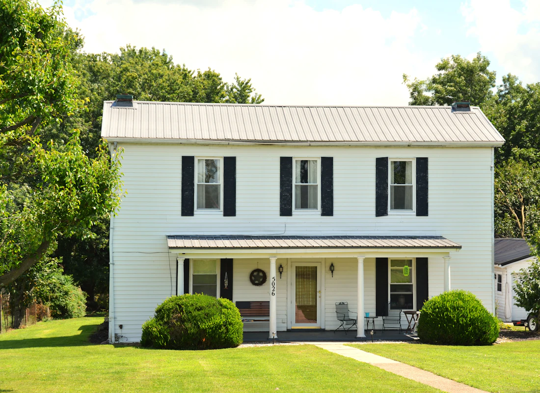 White two-story farmhouse with black shutters and a front porch