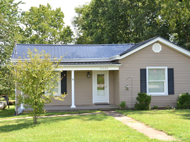 A single story house with beige siding and a dark metal roof