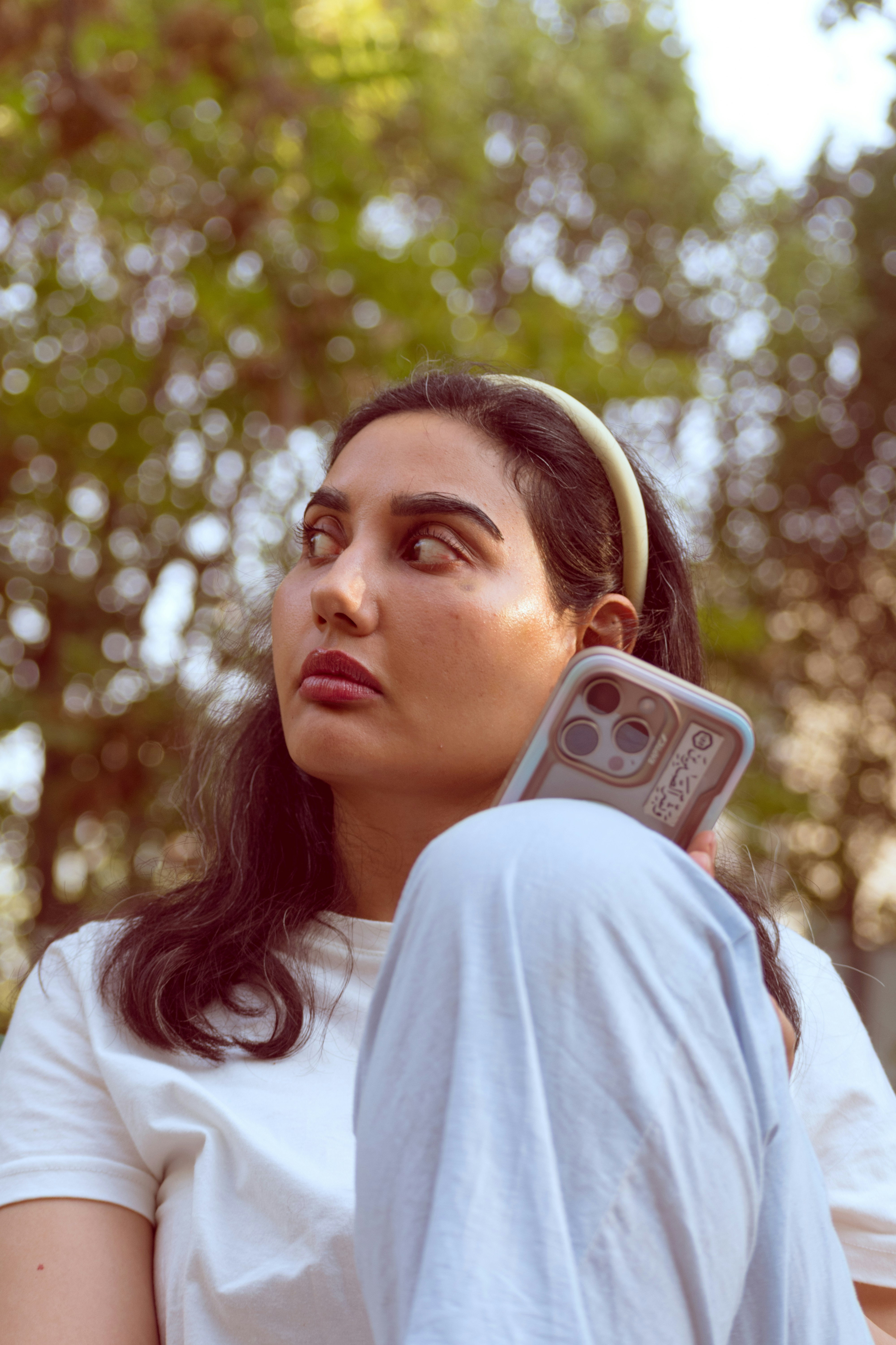 A woman with a headband holding a smartphone against a blurred green tree background
