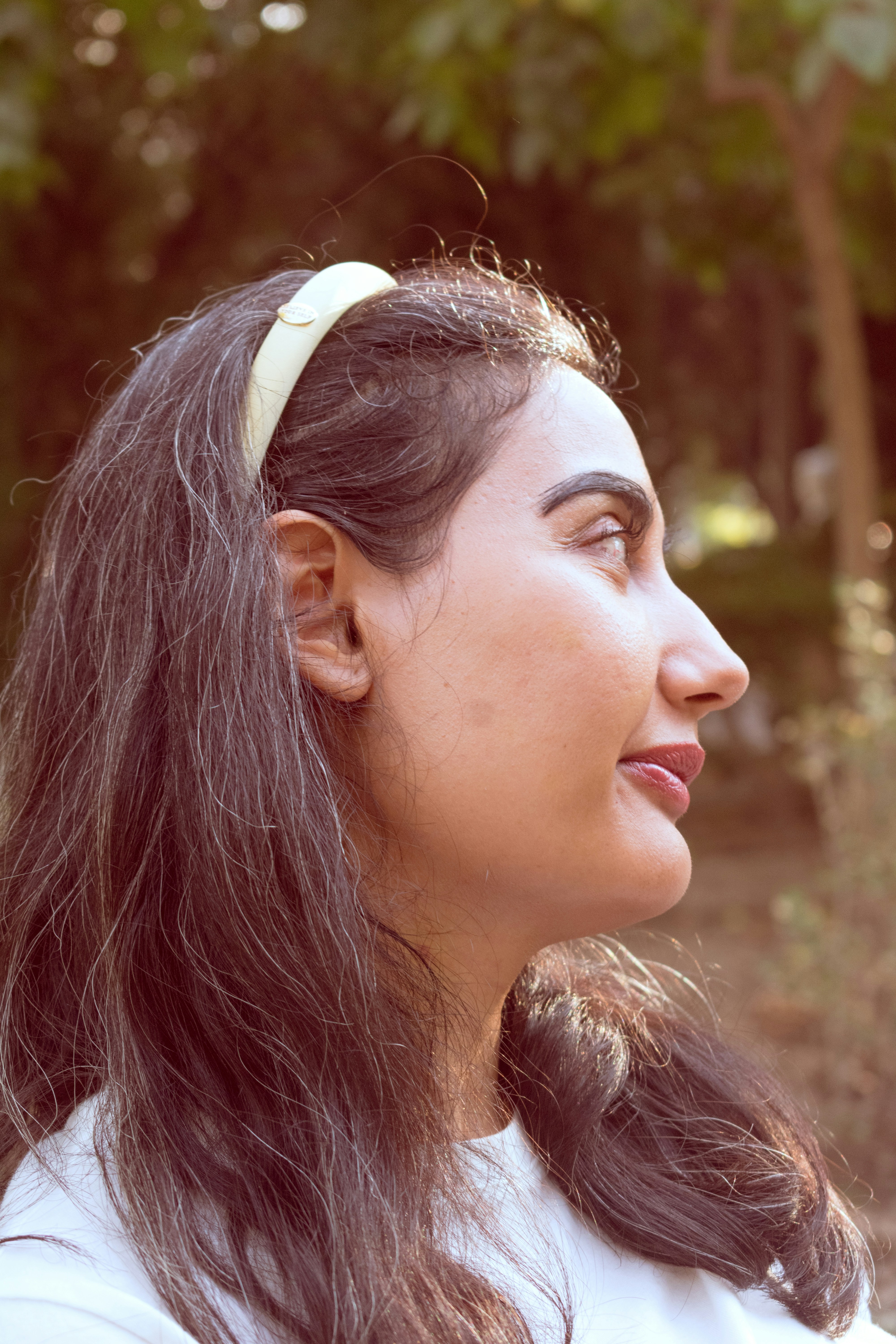 A woman with long dark hair and a cream headband in profile