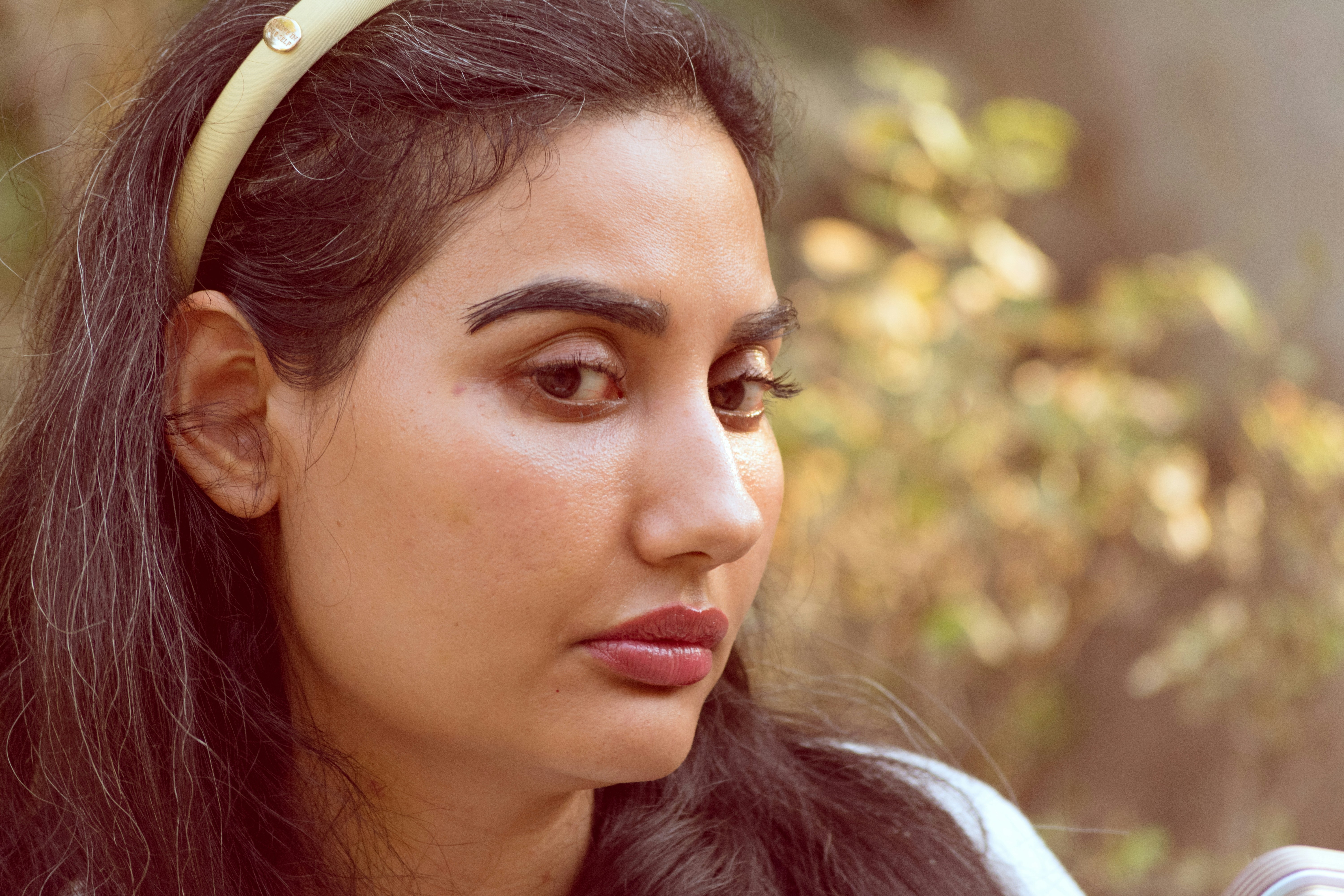 A woman with dark hair and a cream headband looking away in soft light