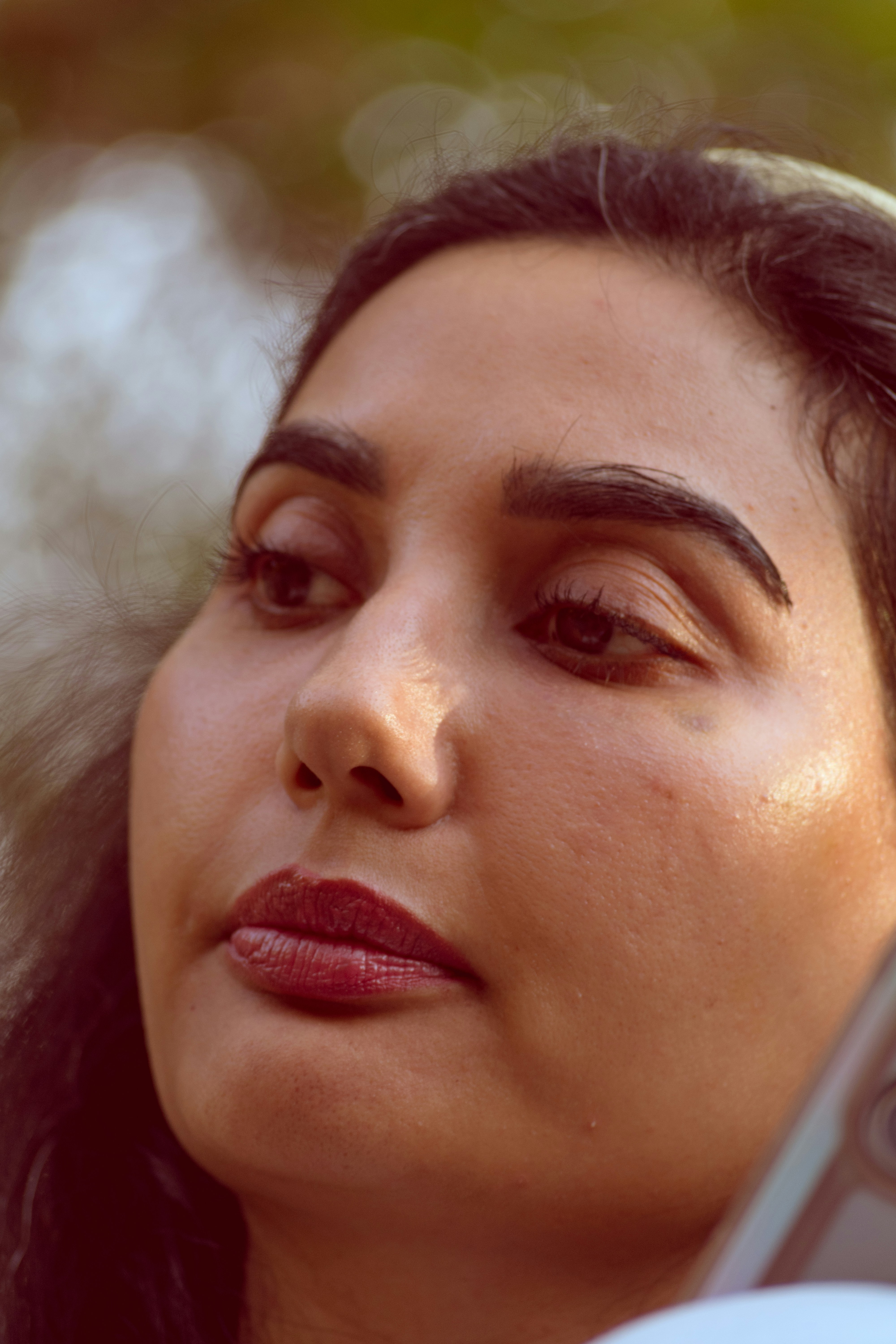 A woman with dark hair and red lipstick looking away in soft light