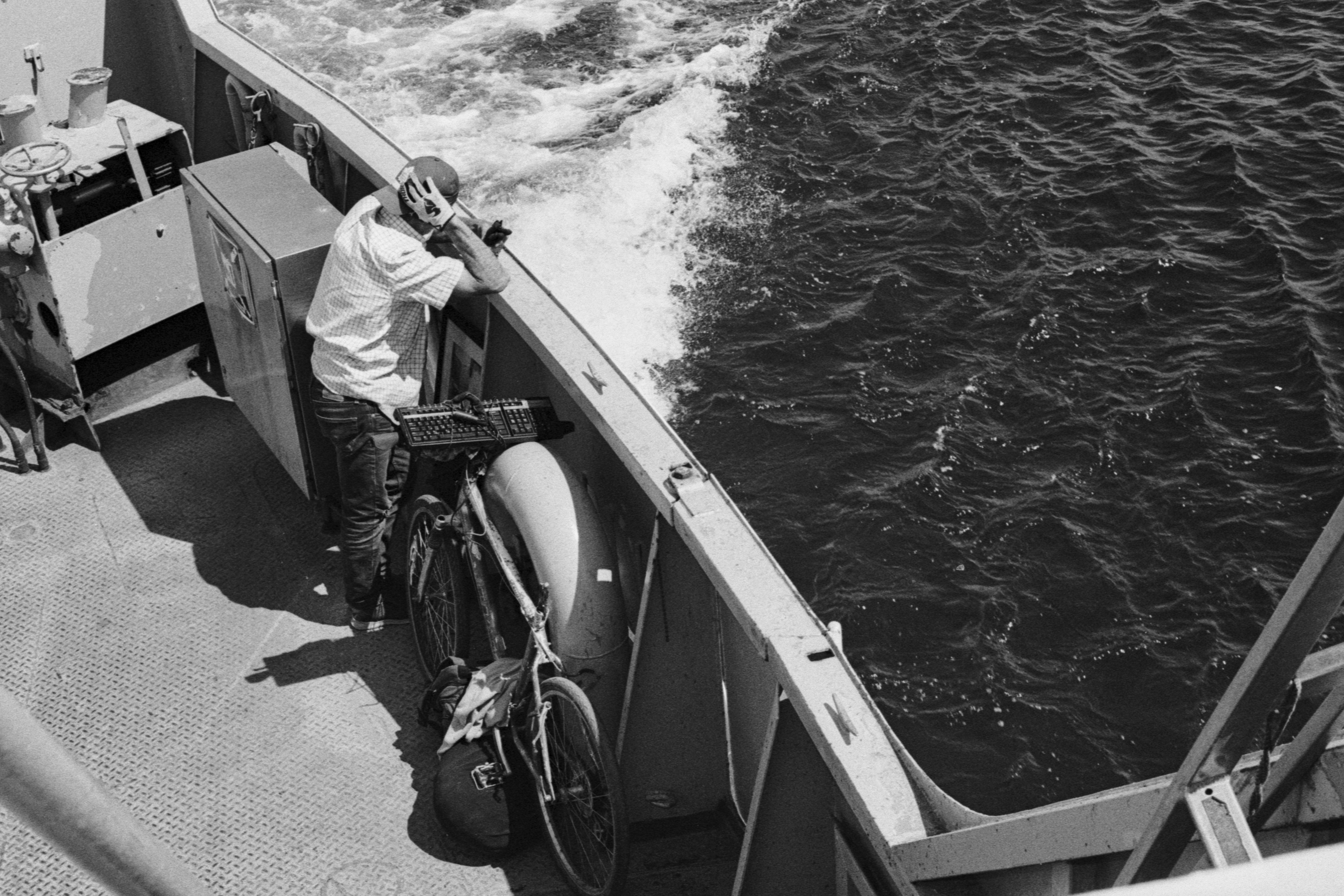 A person leaning on the railing of a ferry with a bicycle nearby