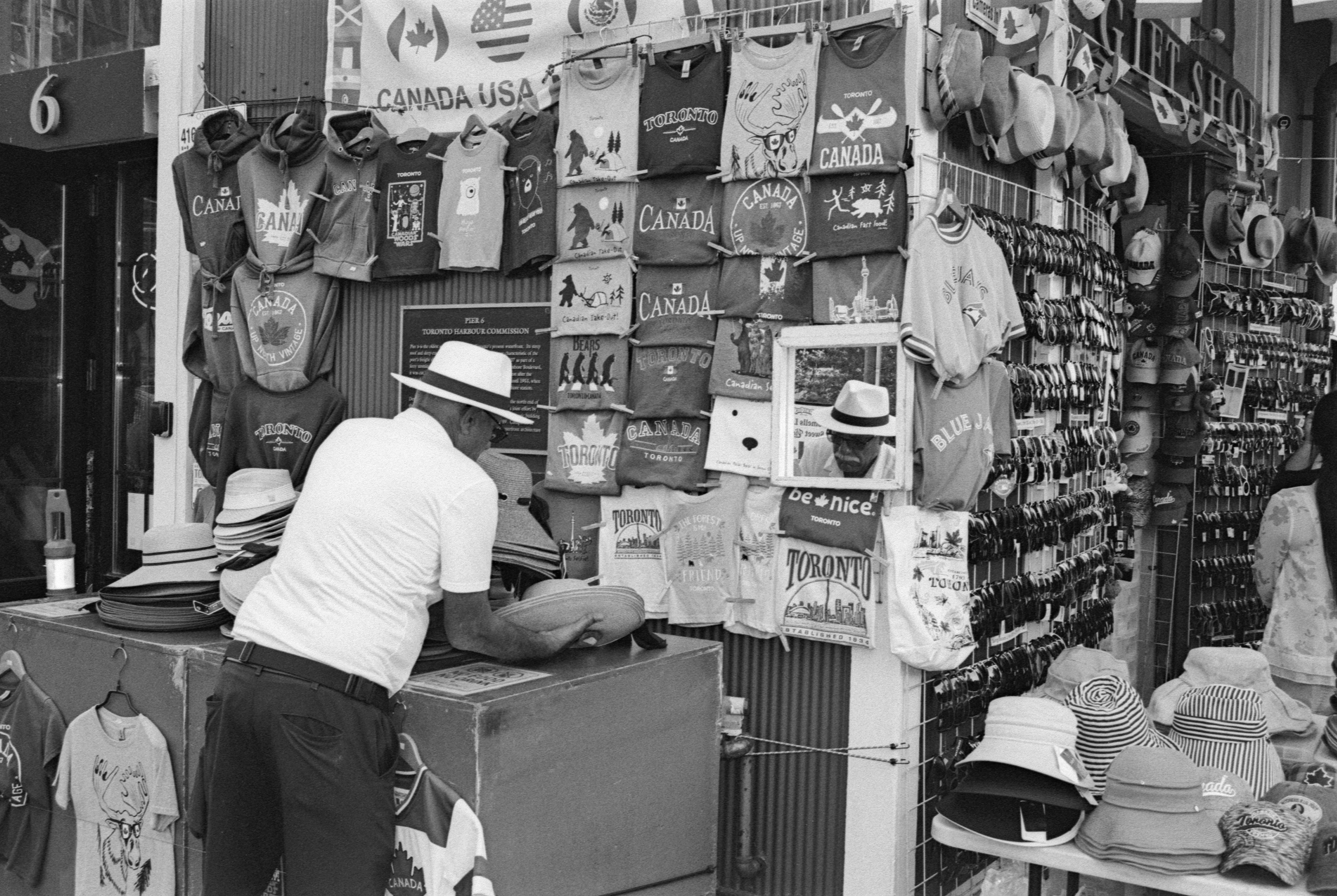 A man in a fedora browsing souvenir t-shirts at a street stall in Toronto