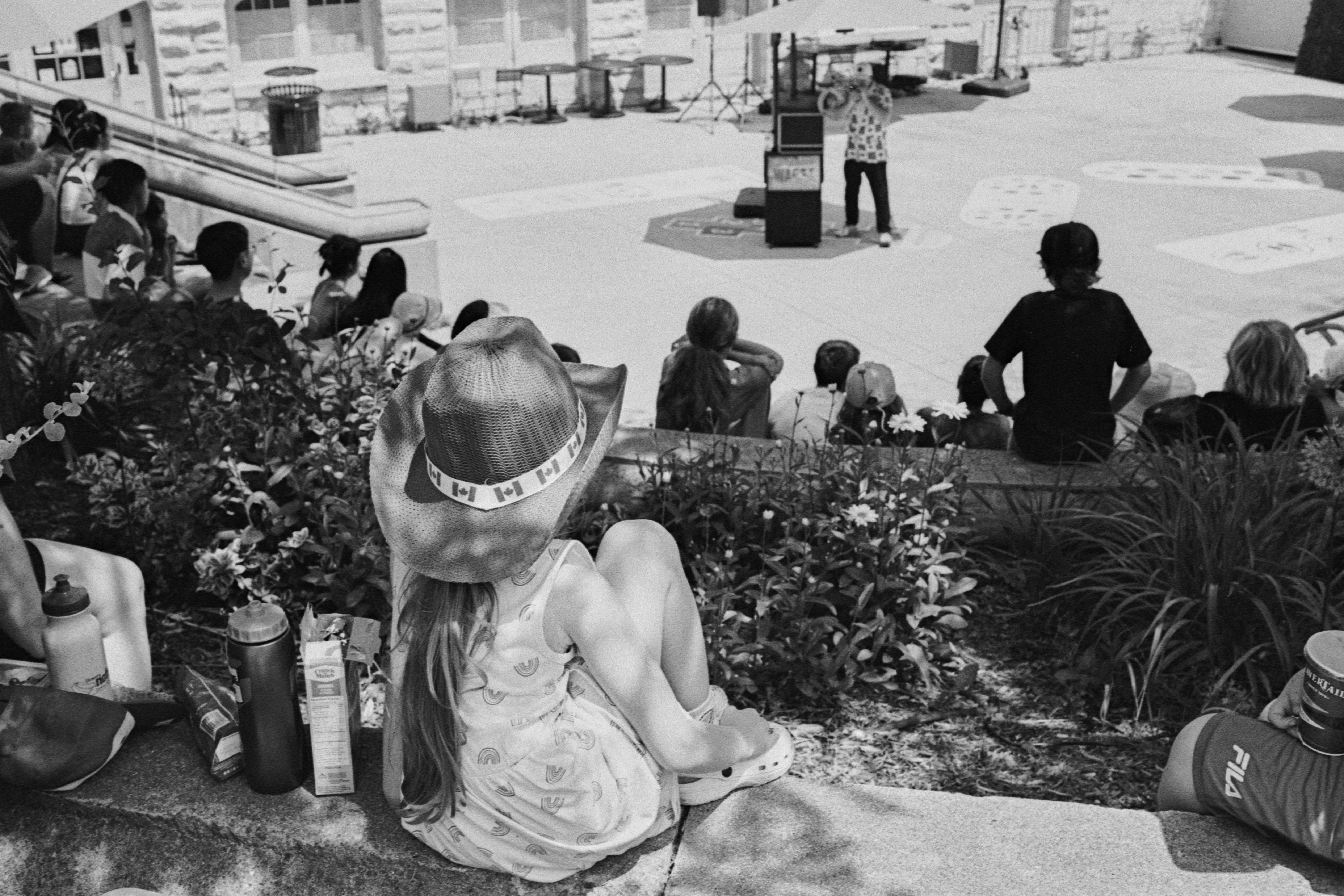 A child in a cowboy hat watching a street performer in a plaza