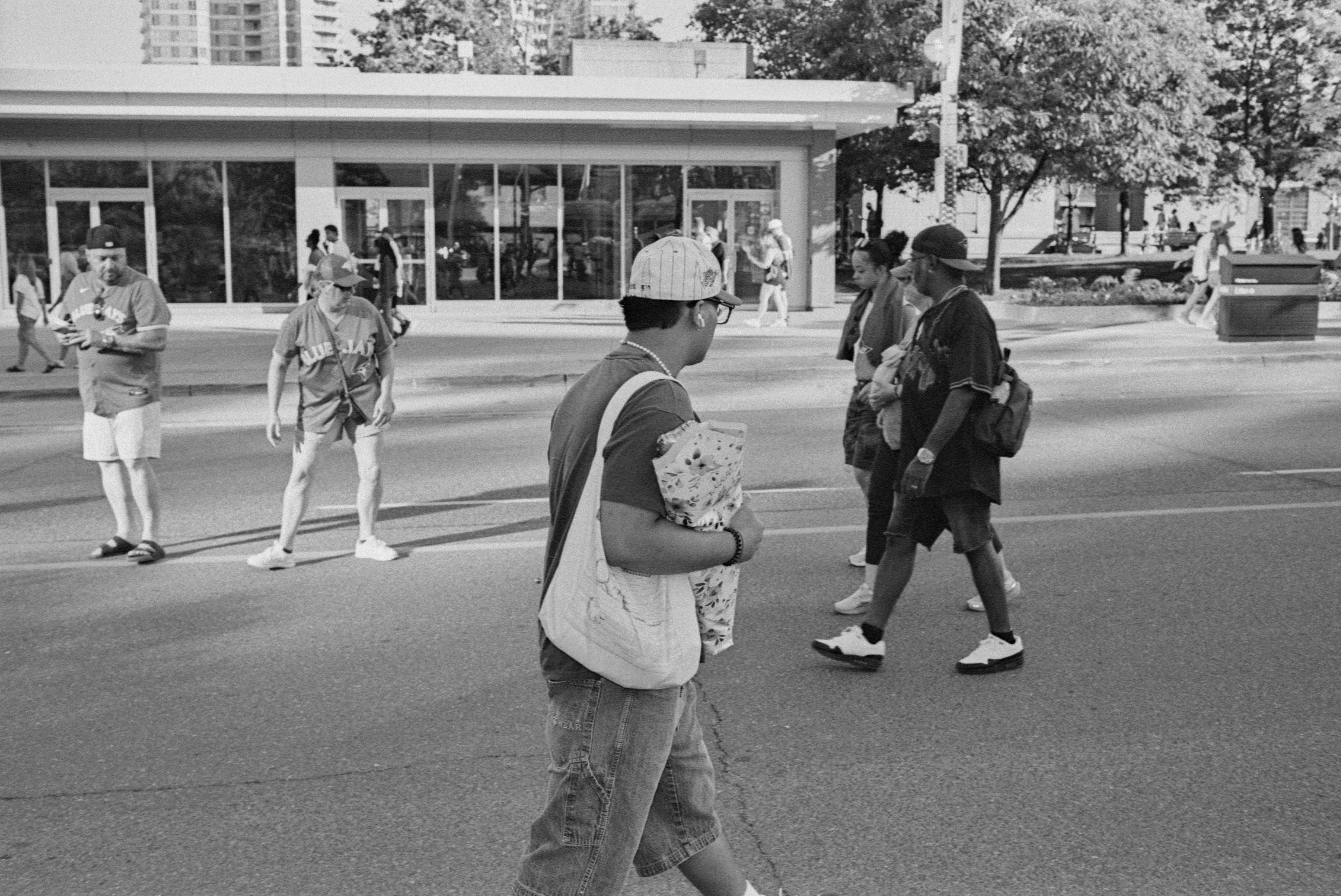 People walking across a city street in front of a modern glass building