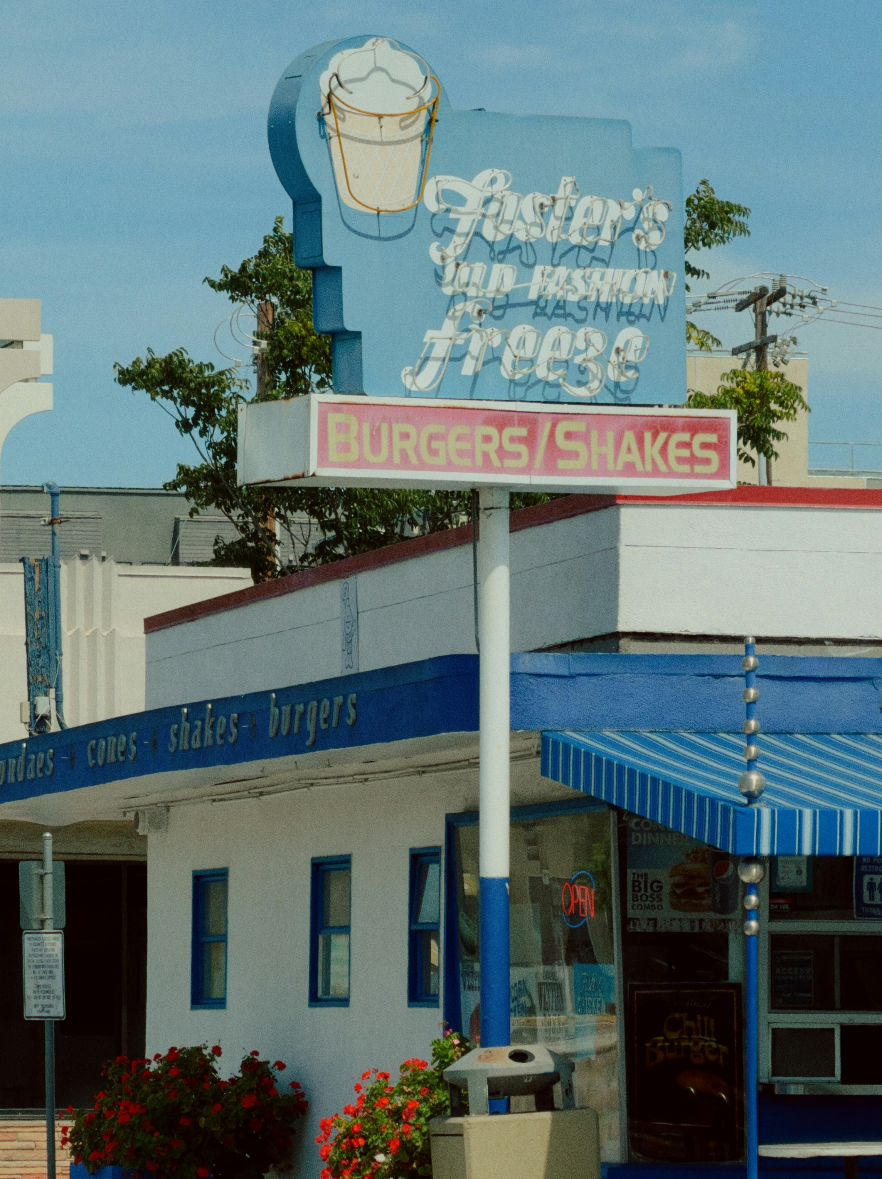 A Foster's Freeze restaurant sign above a white building with blue trim and flowers