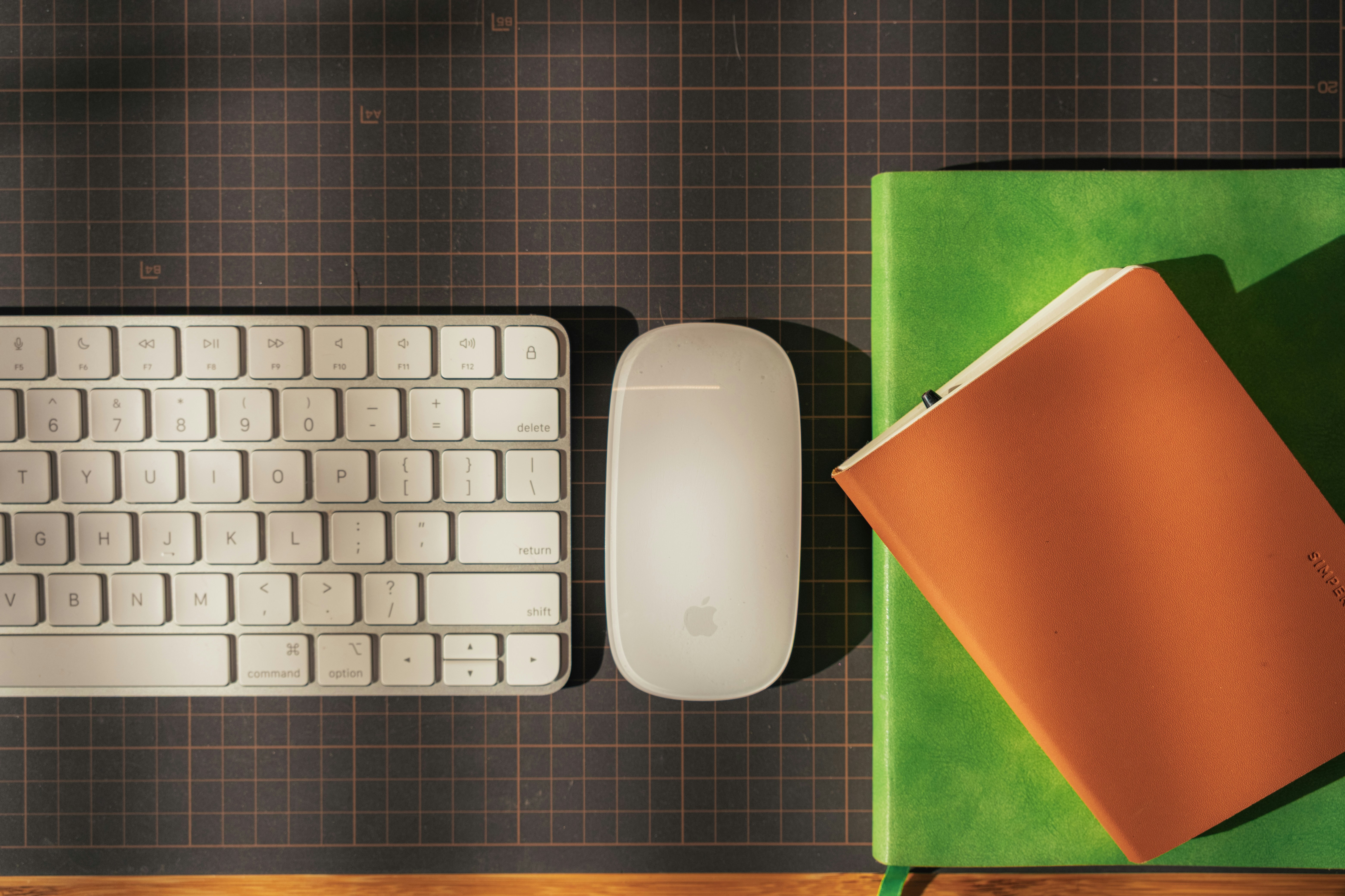 A wireless keyboard, a computer mouse, and a notebook on a dark grid mat