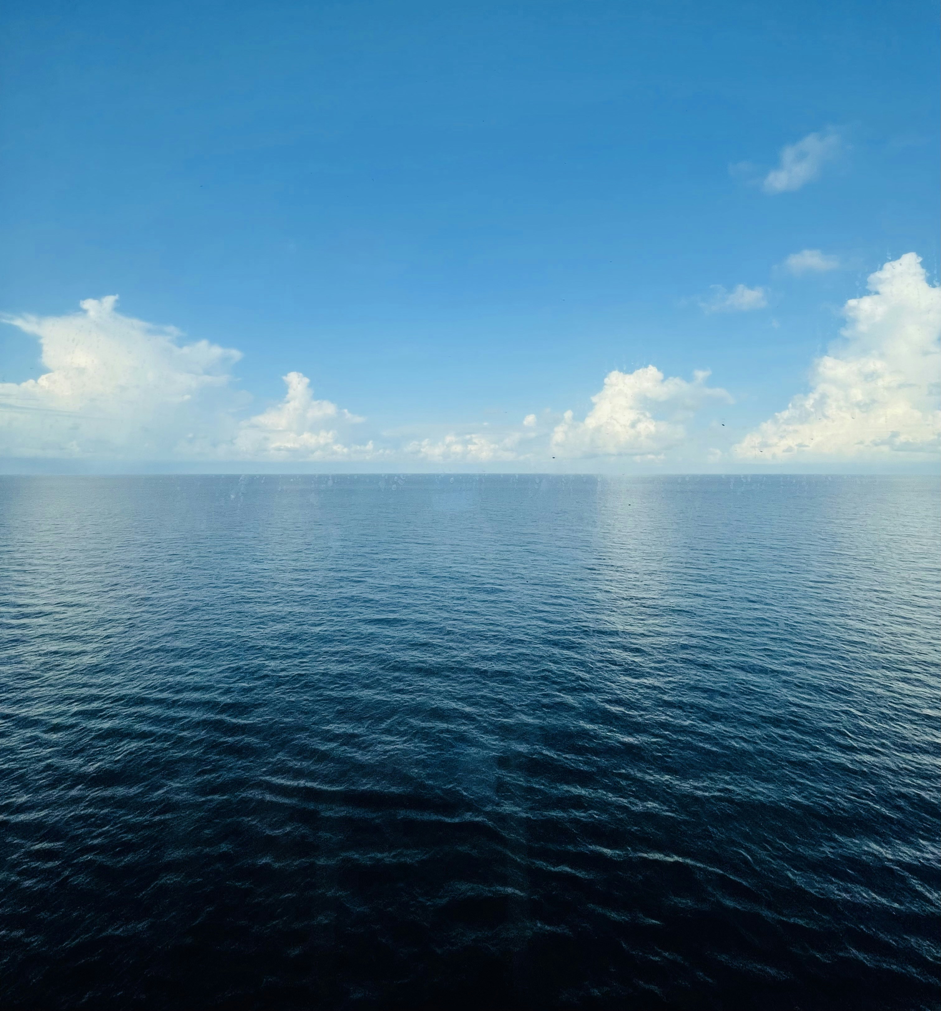 A calm blue ocean under a bright sky with scattered white clouds