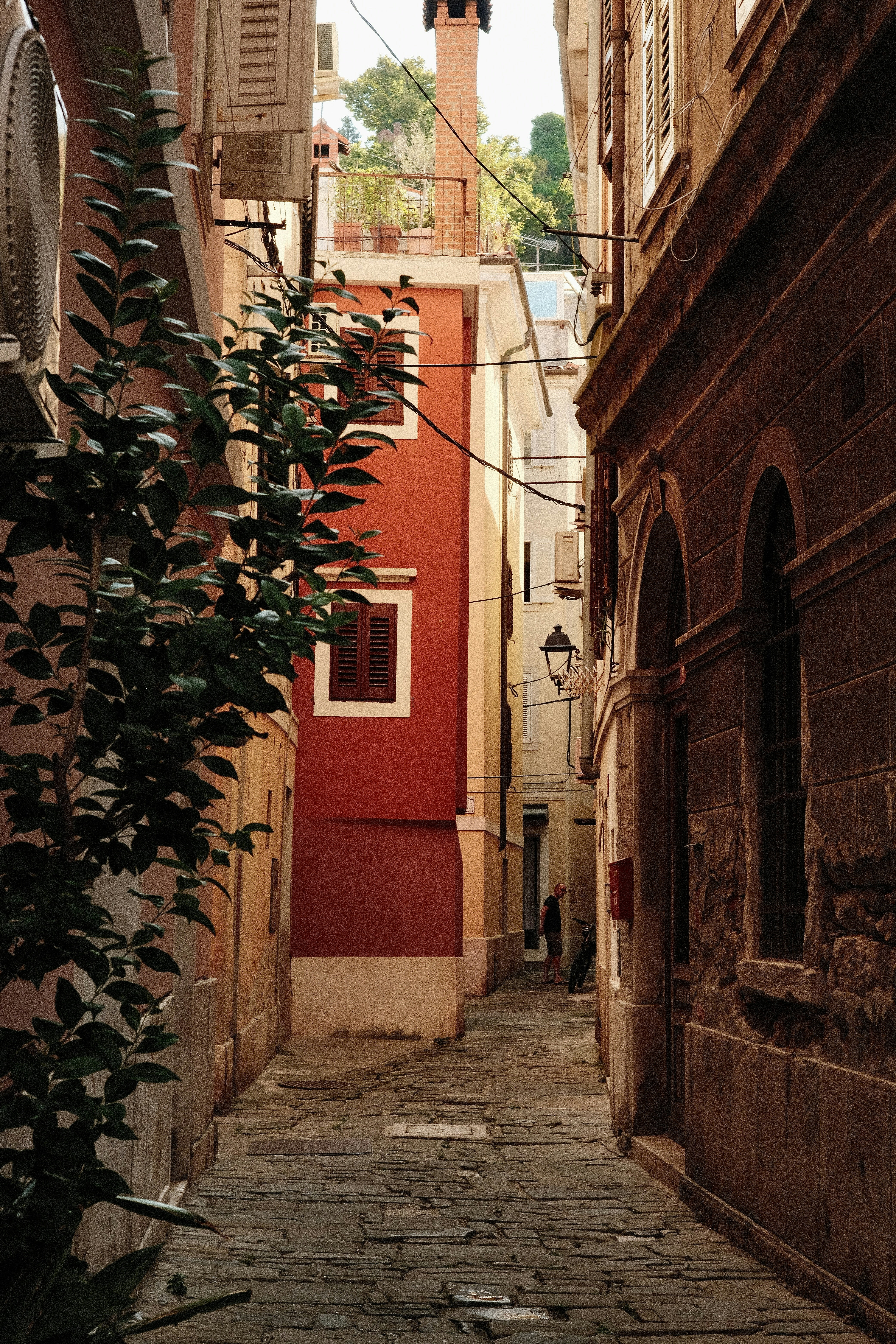 A narrow stone alleyway between tall colorful buildings with a person in the distance