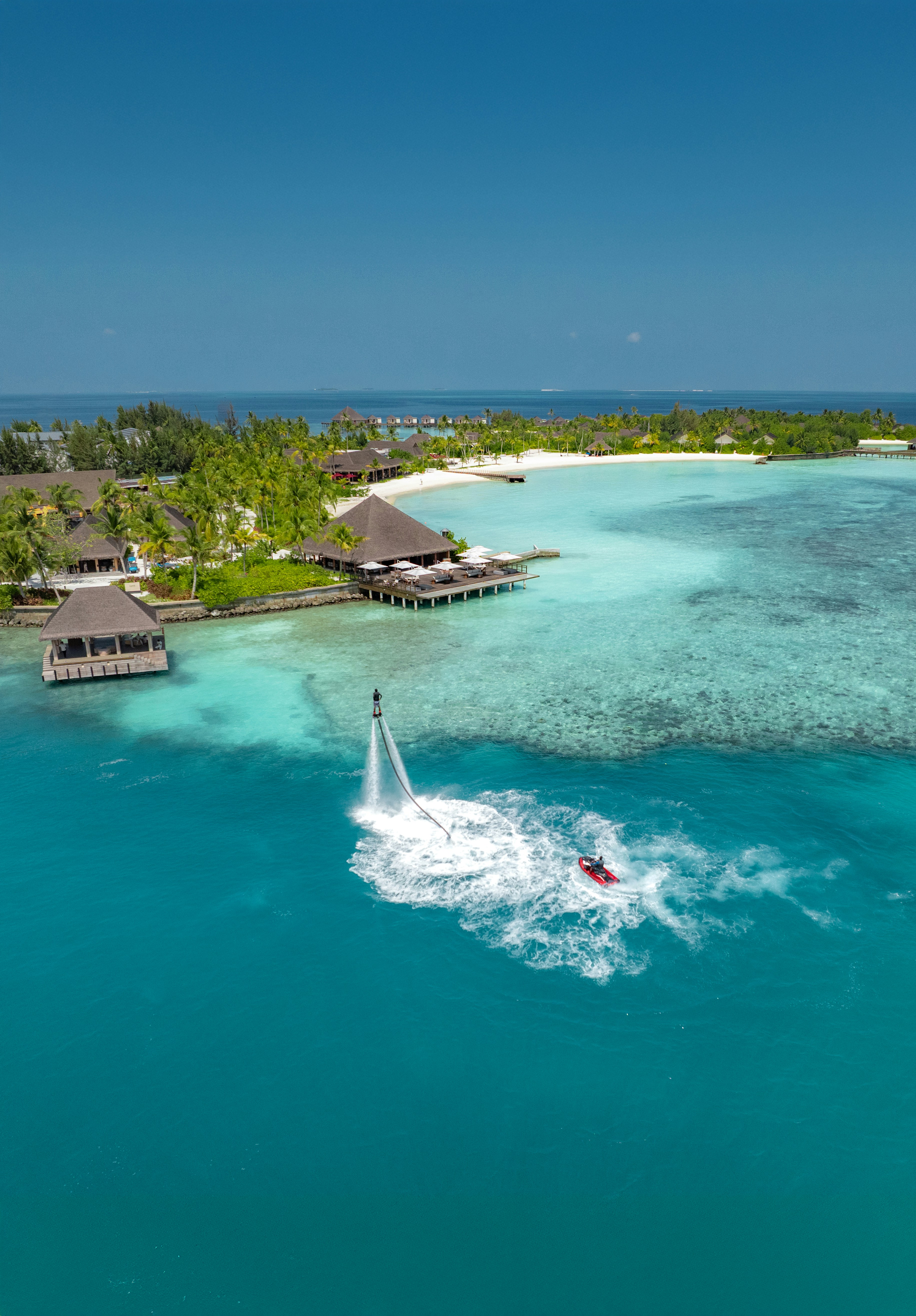 A person flyboarding above turquoise water near a tropical island resort