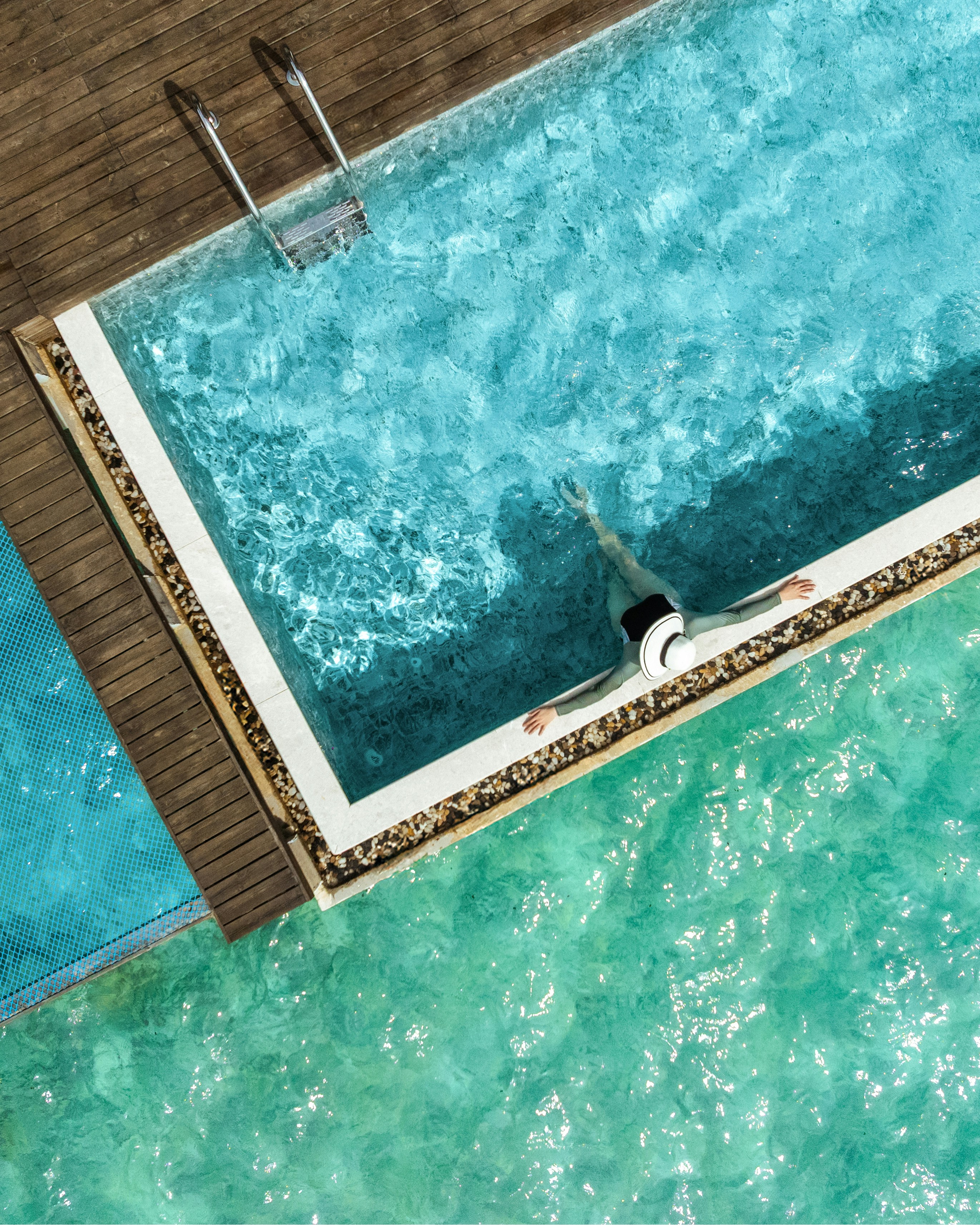 Aerial view of a person in a hat relaxing in a swimming pool