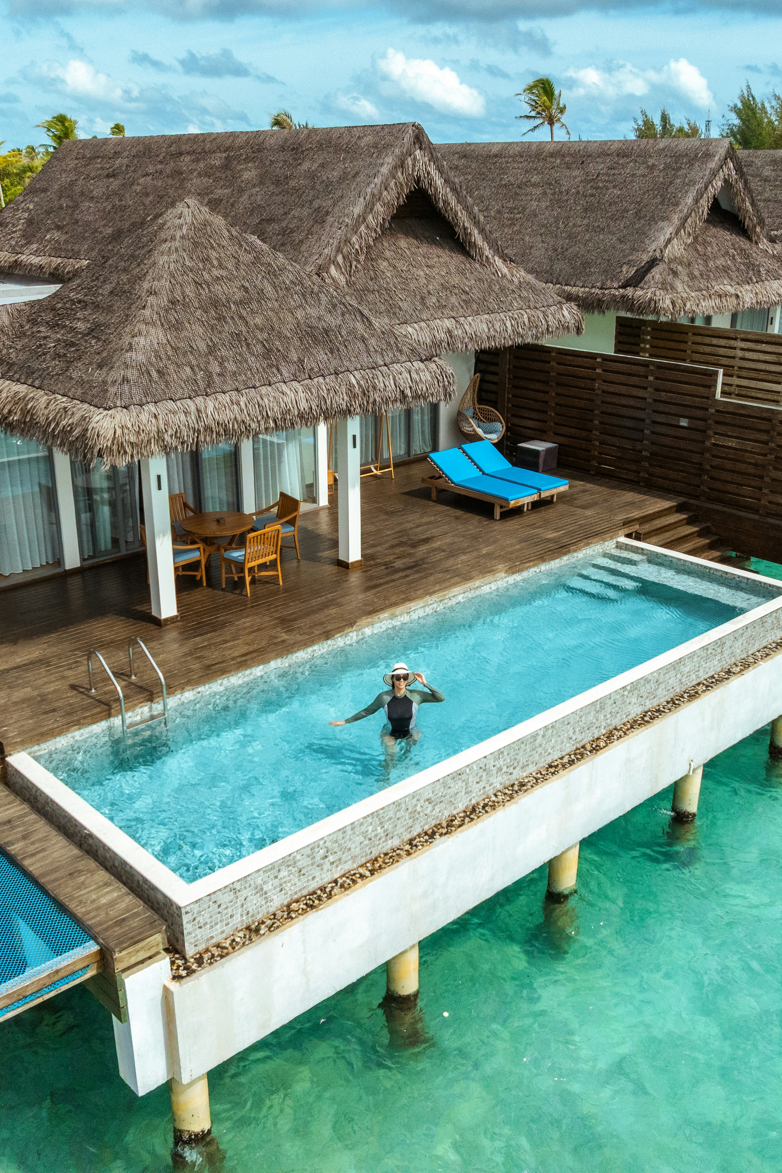 A woman in a swimsuit and hat standing in an overwater villa pool