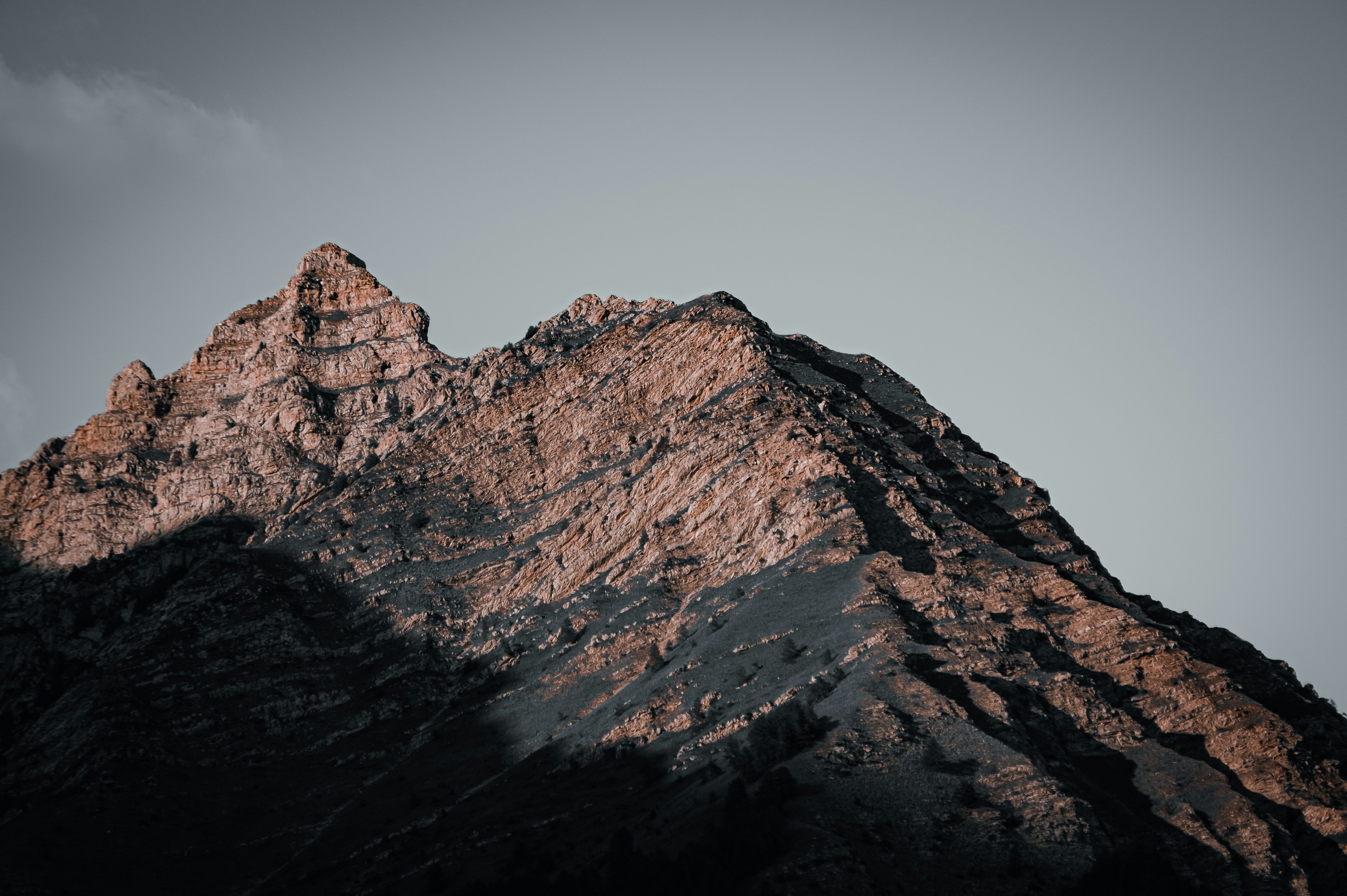 A rugged mountain peak with rocky textures under a clear grey sky