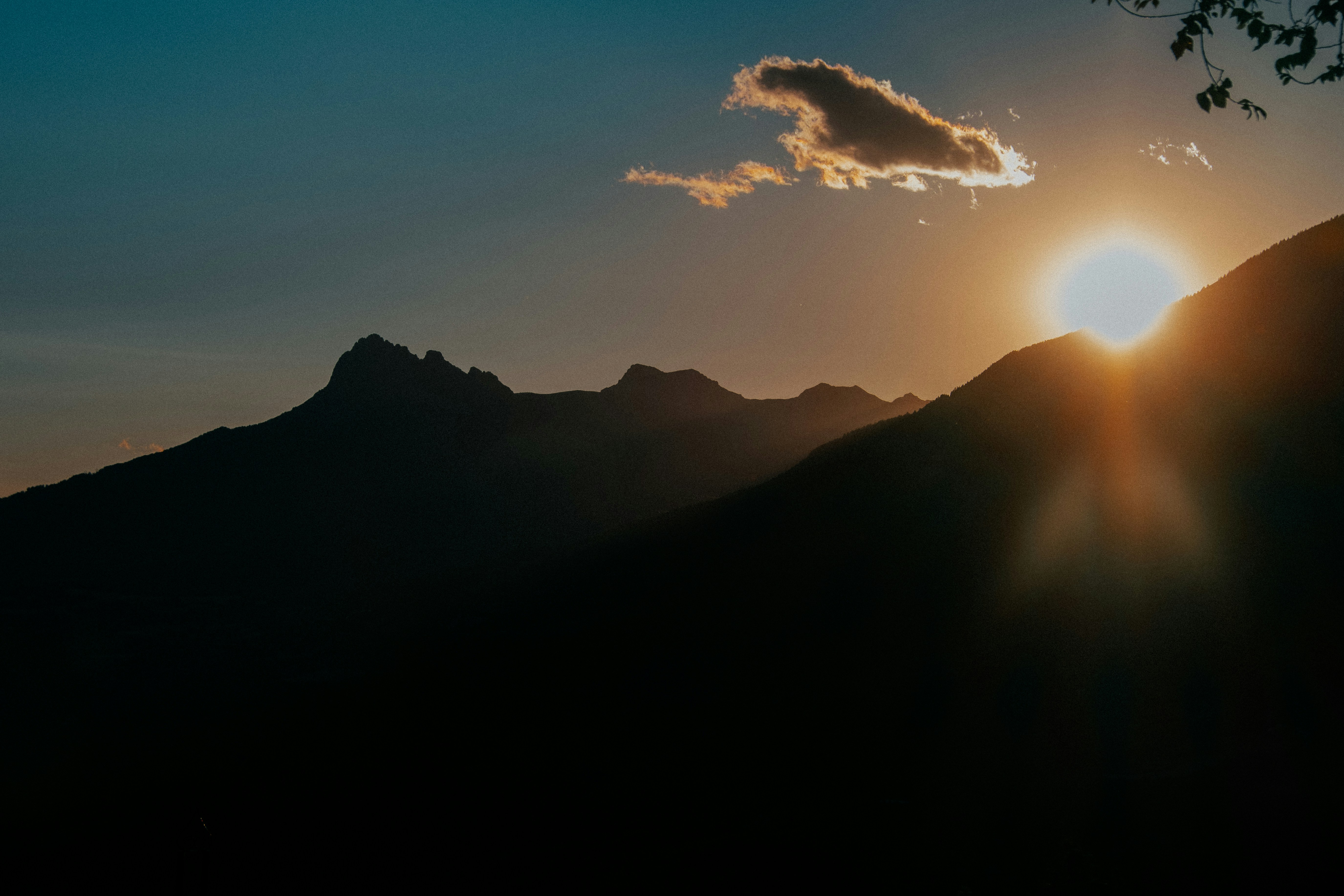 Low sun behind dark mountain silhouettes with a small cloud in the sky