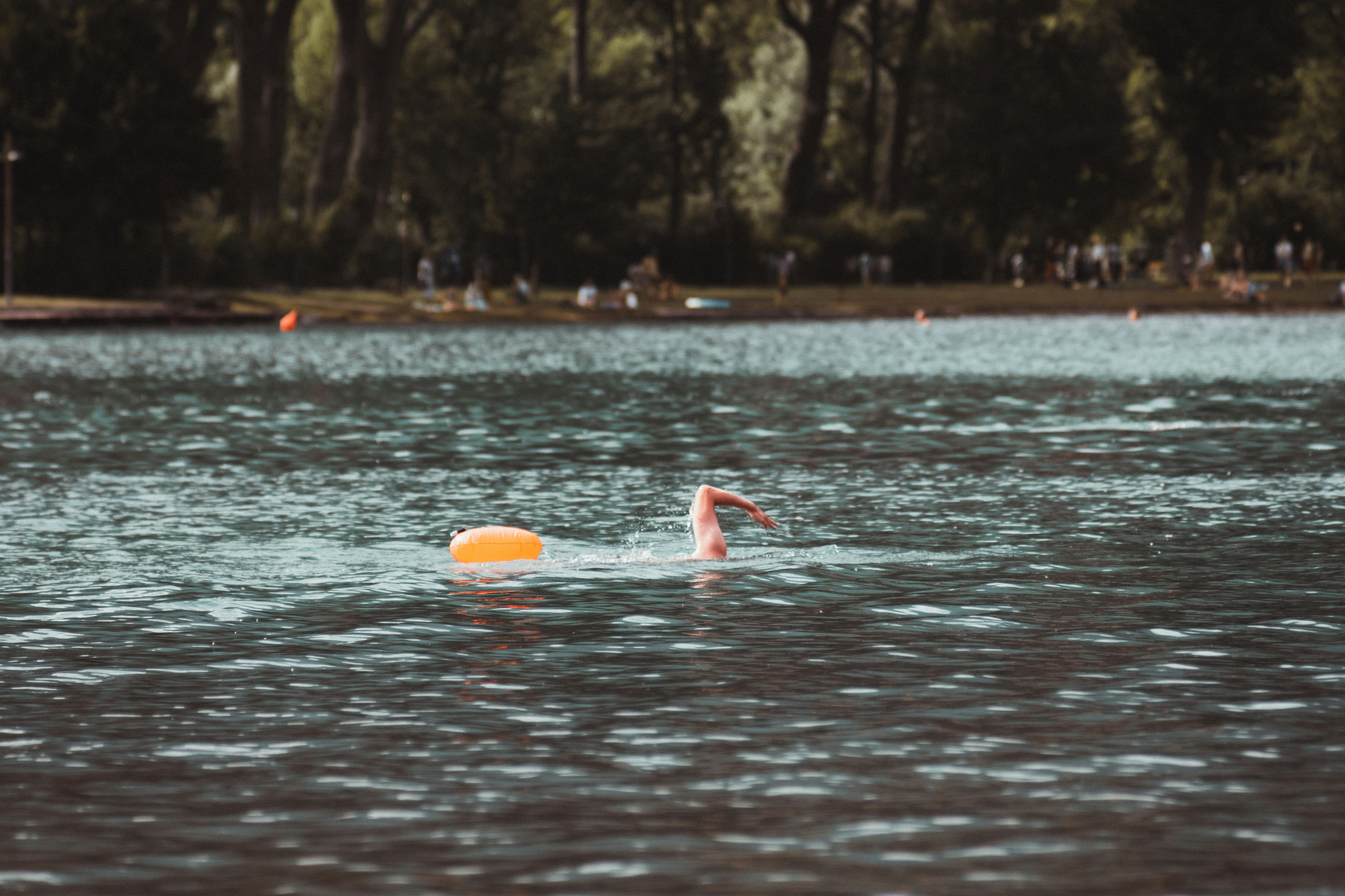 A person swimming in a lake with an orange tow float