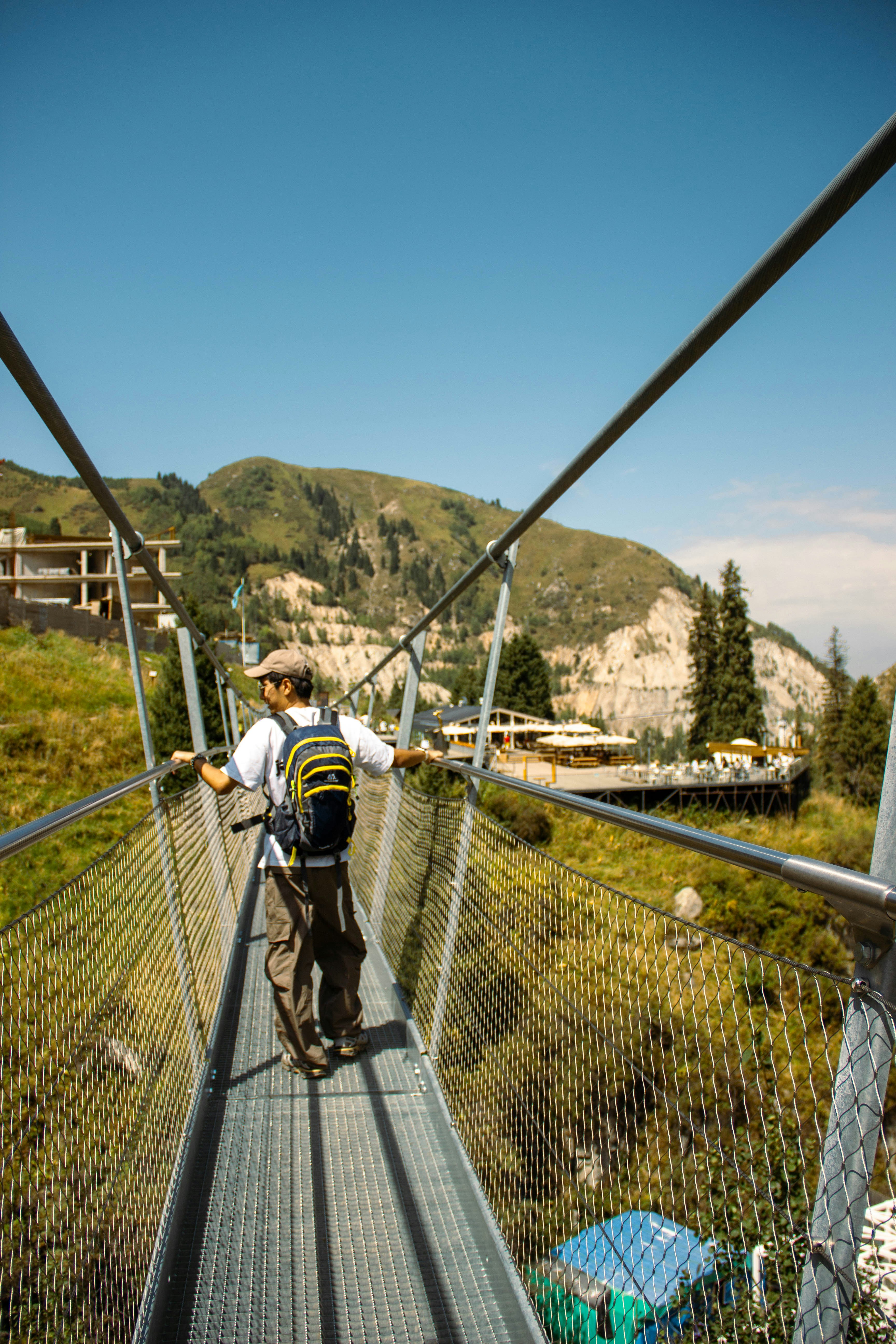 A person with a backpack walking across a metal suspension bridge in the mountains