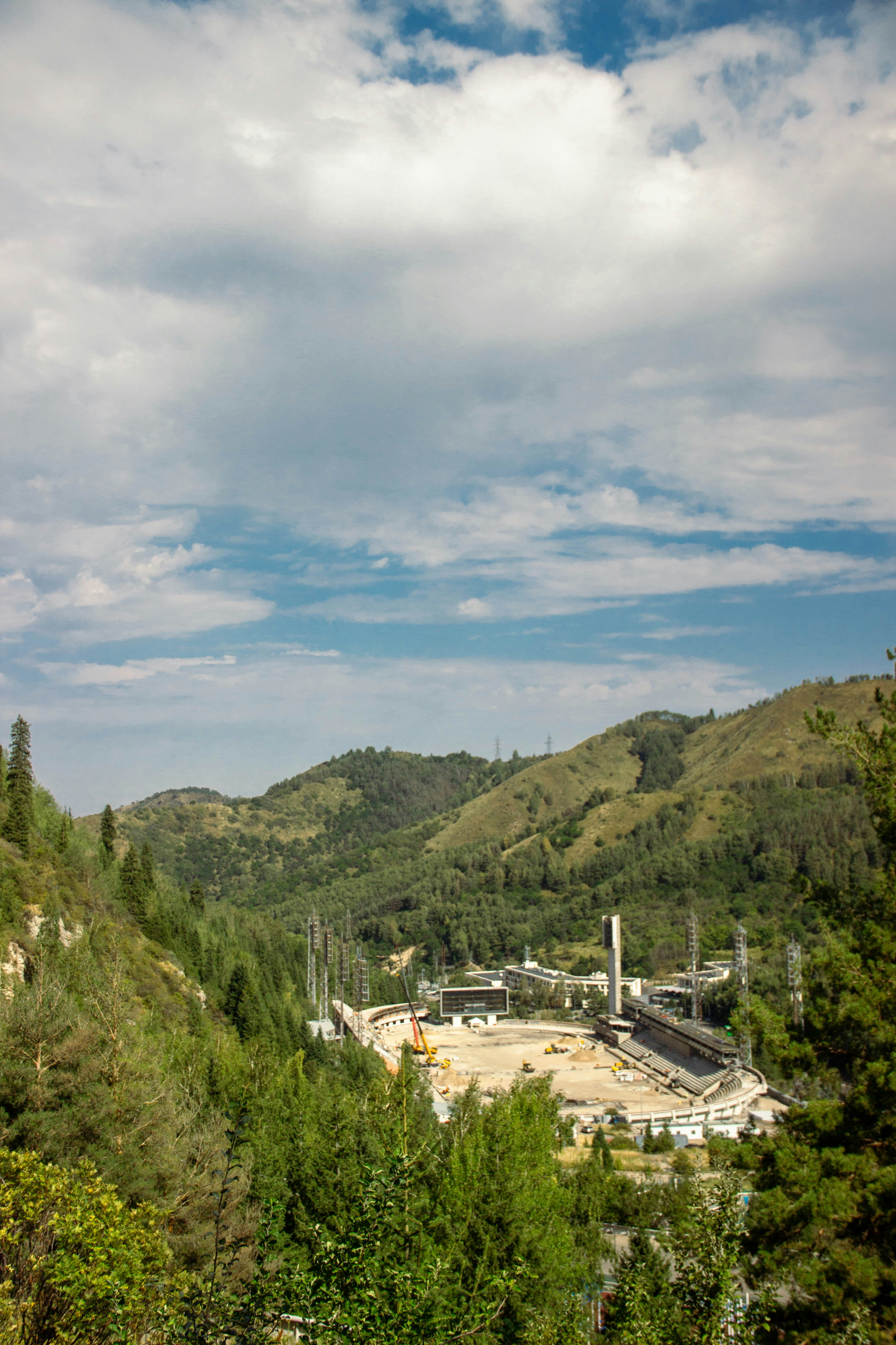 An outdoor stadium in a valley surrounded by green forested mountains under a cloudy sky