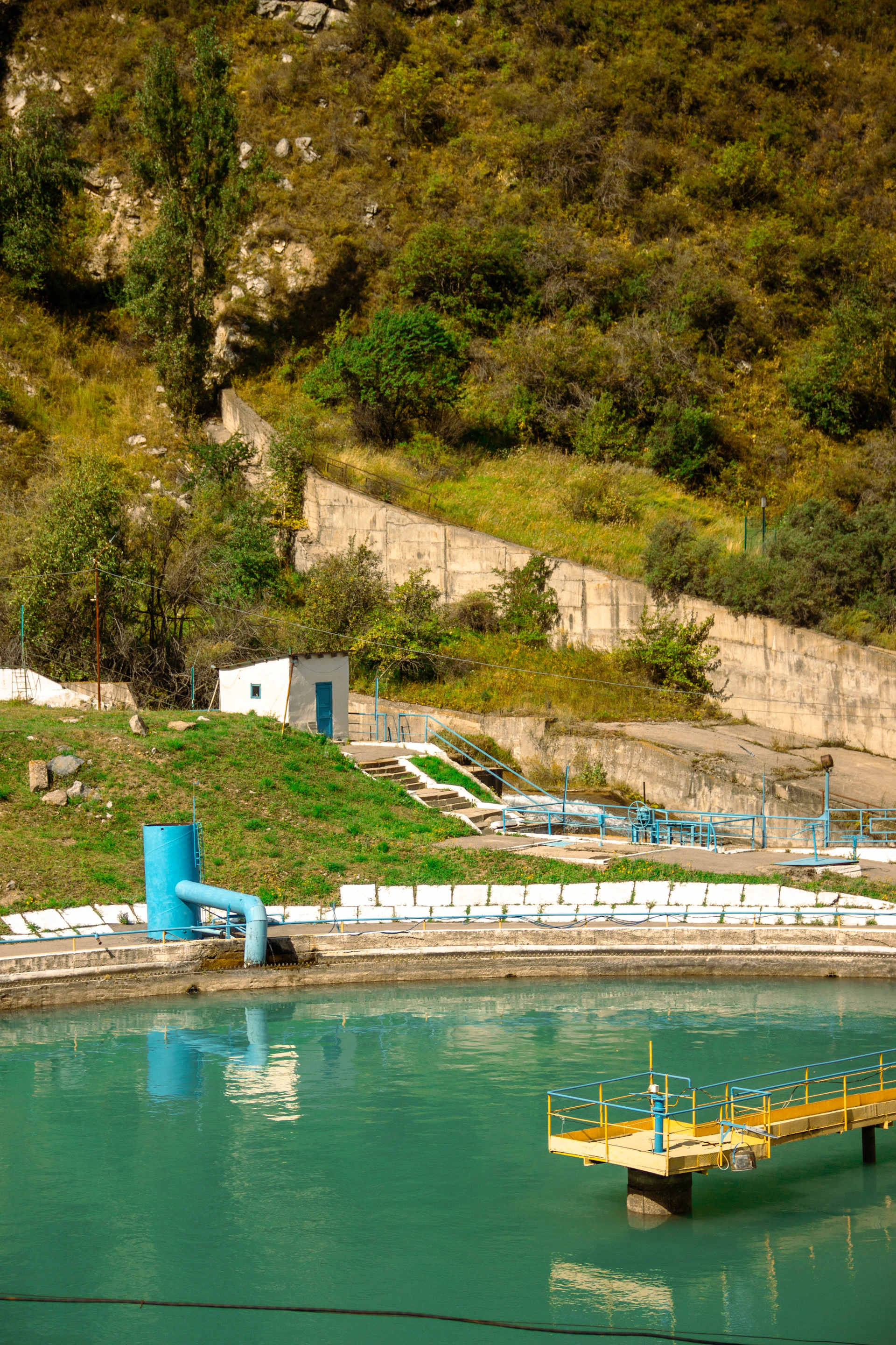 A turquoise water reservoir with a yellow metal platform and a blue pipe