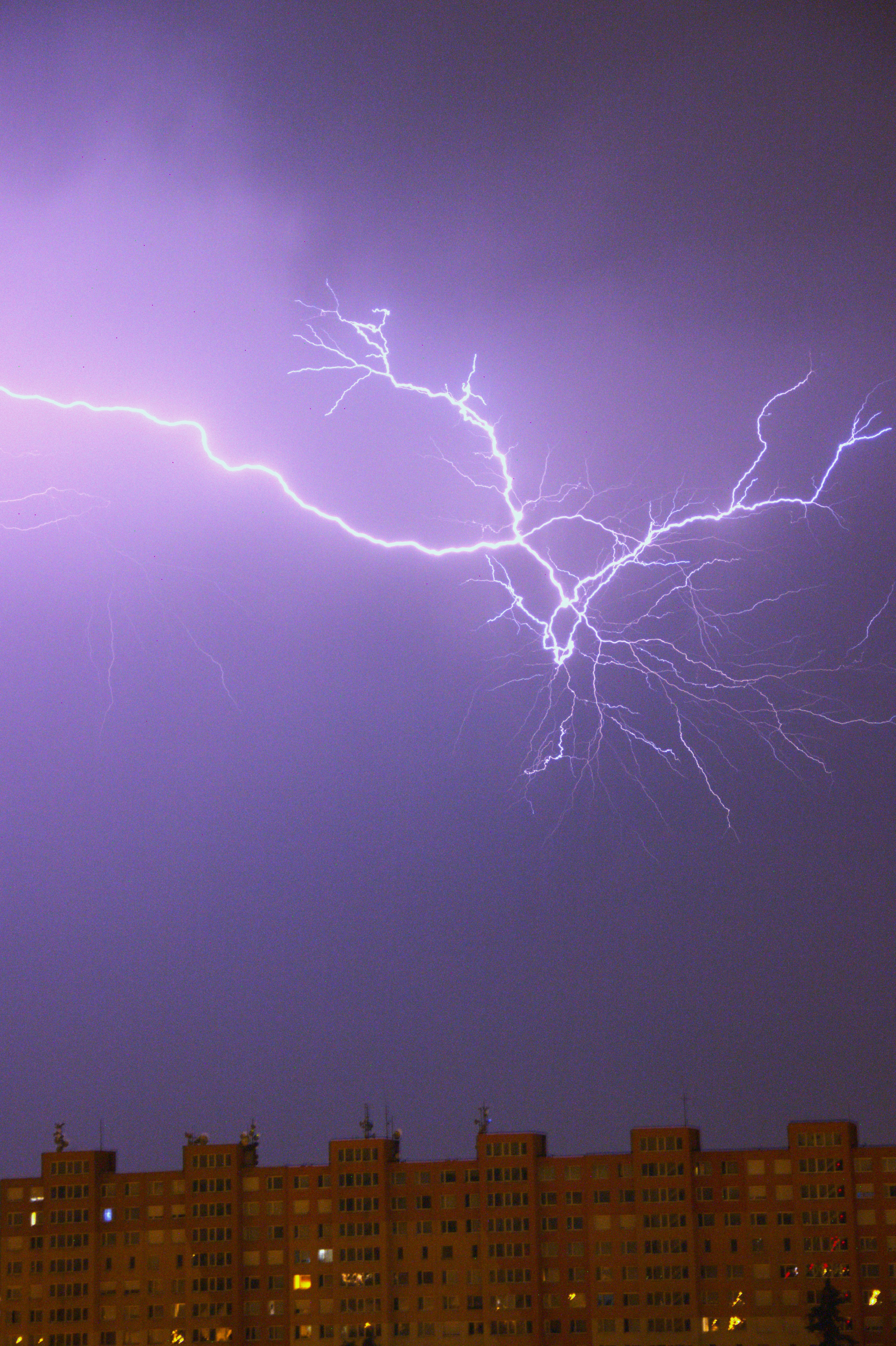 A bright purple lightning bolt striking across a dark sky above an apartment building