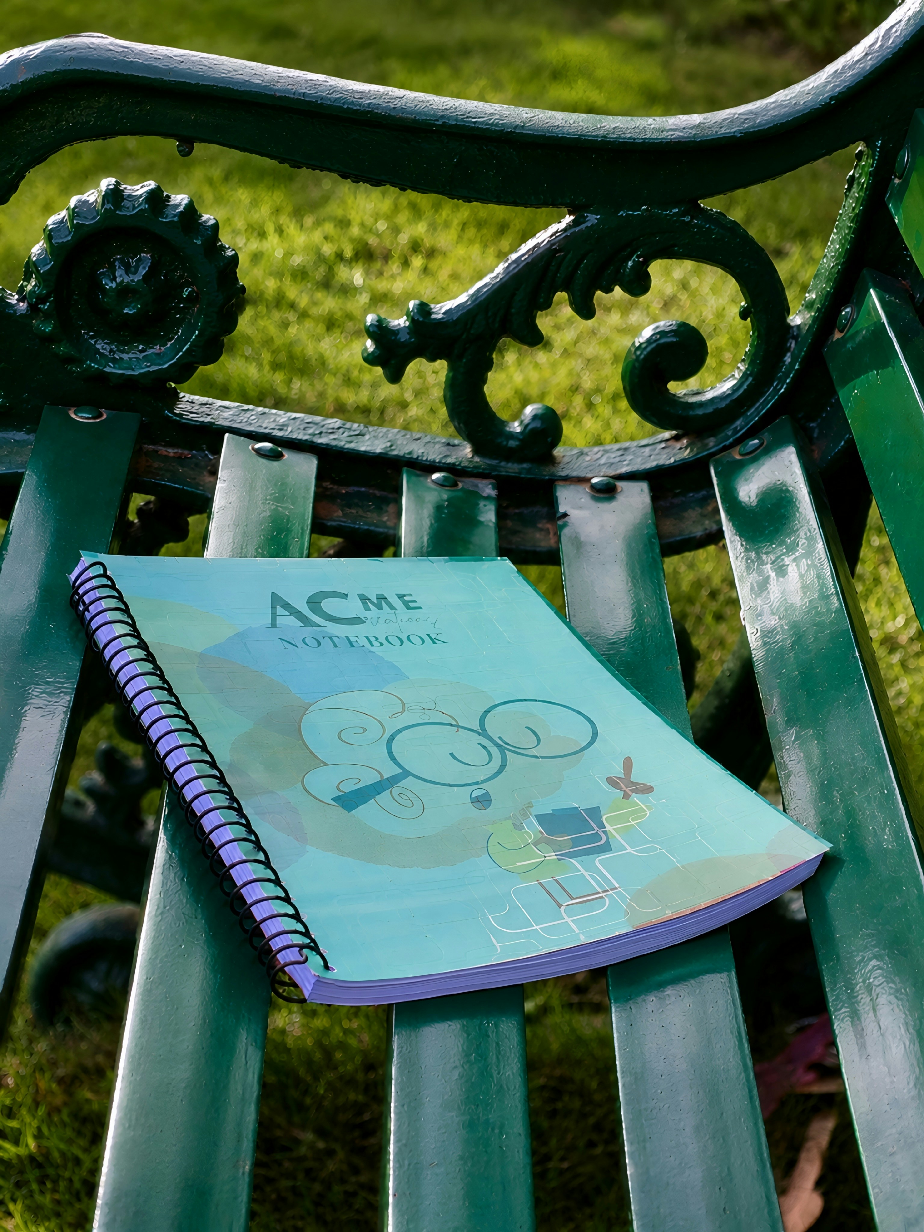 Un cuaderno encuadernado en espiral con una ilustración de dibujos animados sobre un banco metálico verde del parque