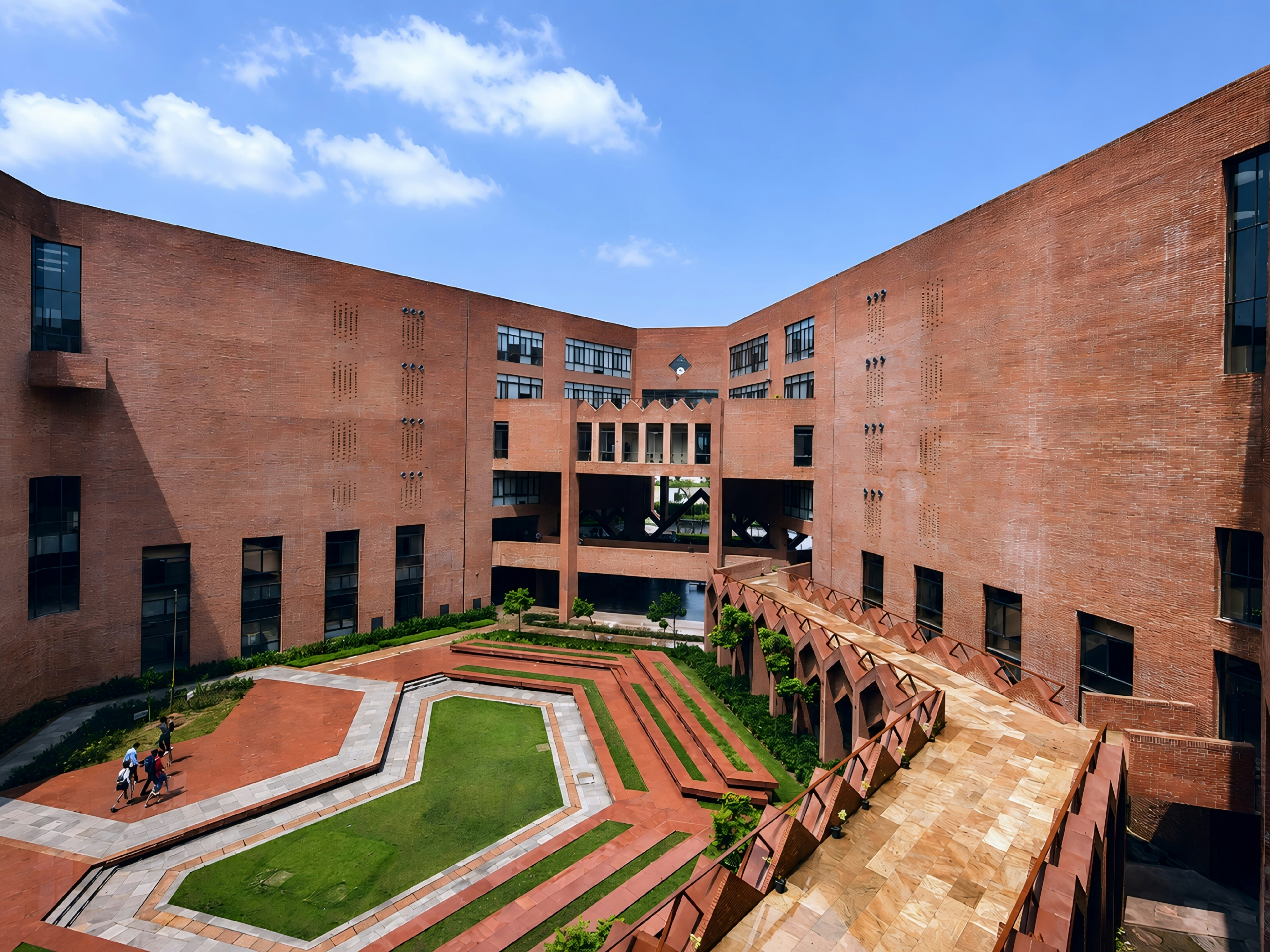 A red brick university courtyard with a green lawn and stone walkways in India