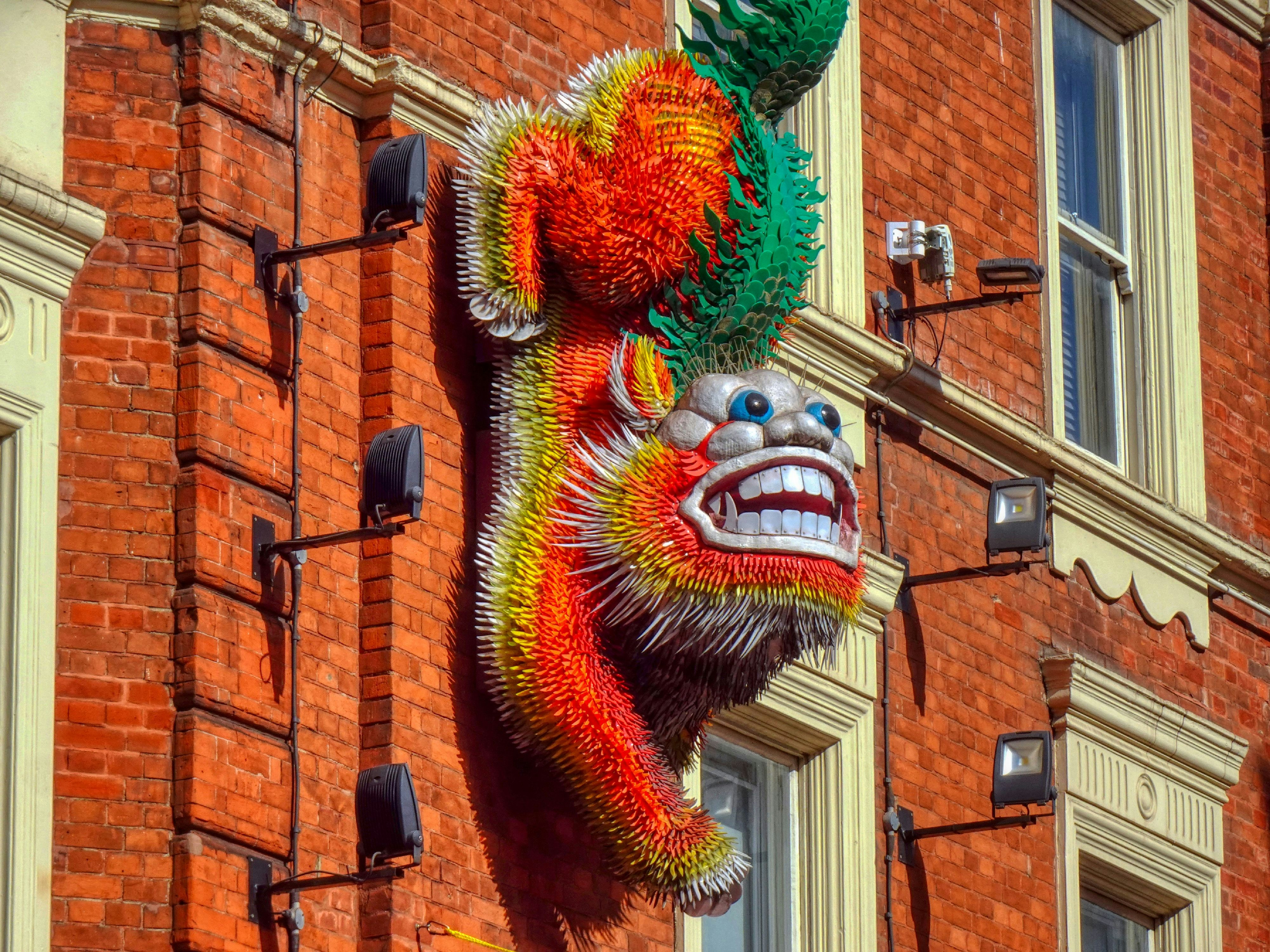 Une sculpture de dragon colorée montée sur un mur de brique rouge