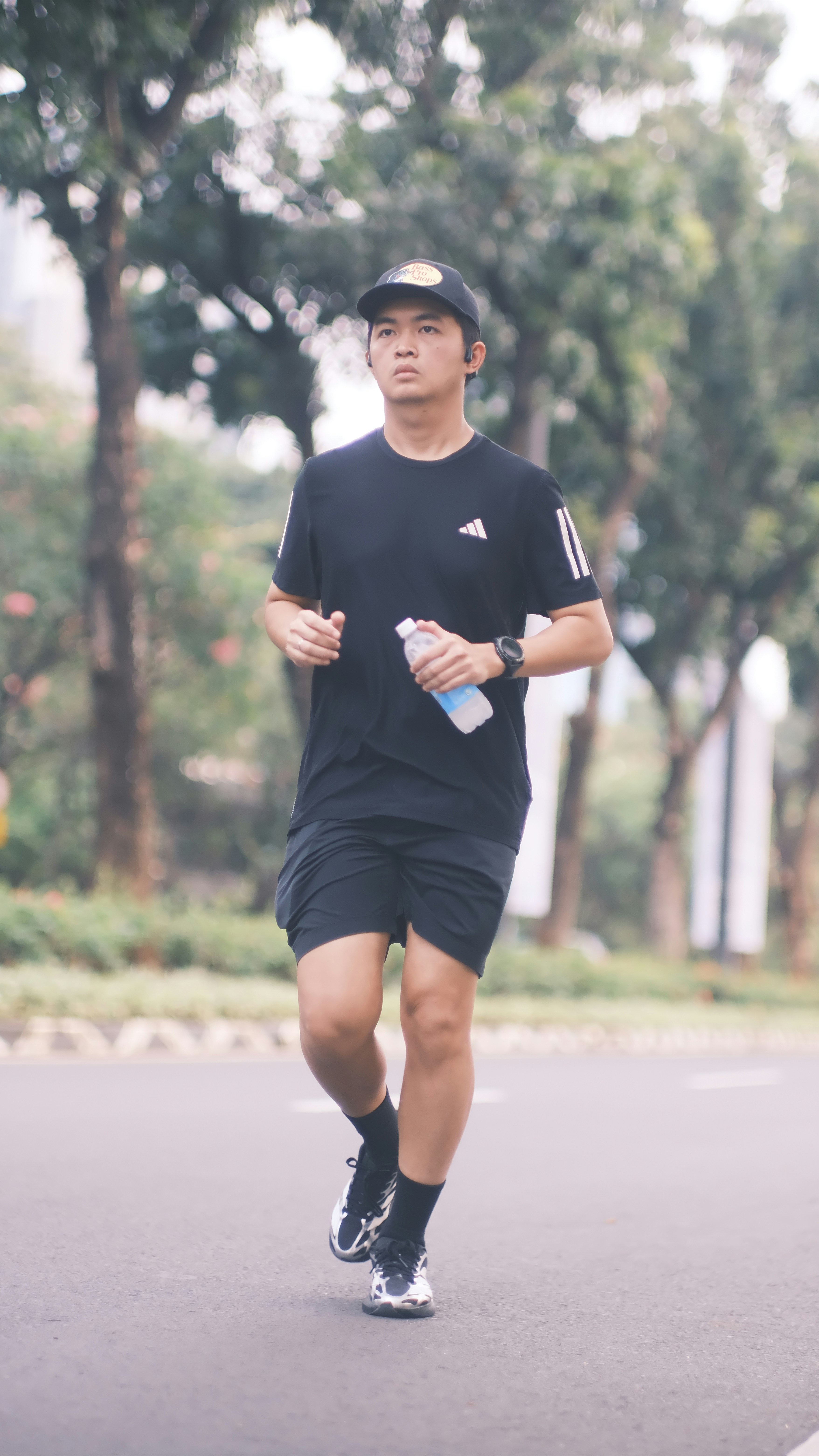 A man in a black t-shirt and cap running on a road holding water