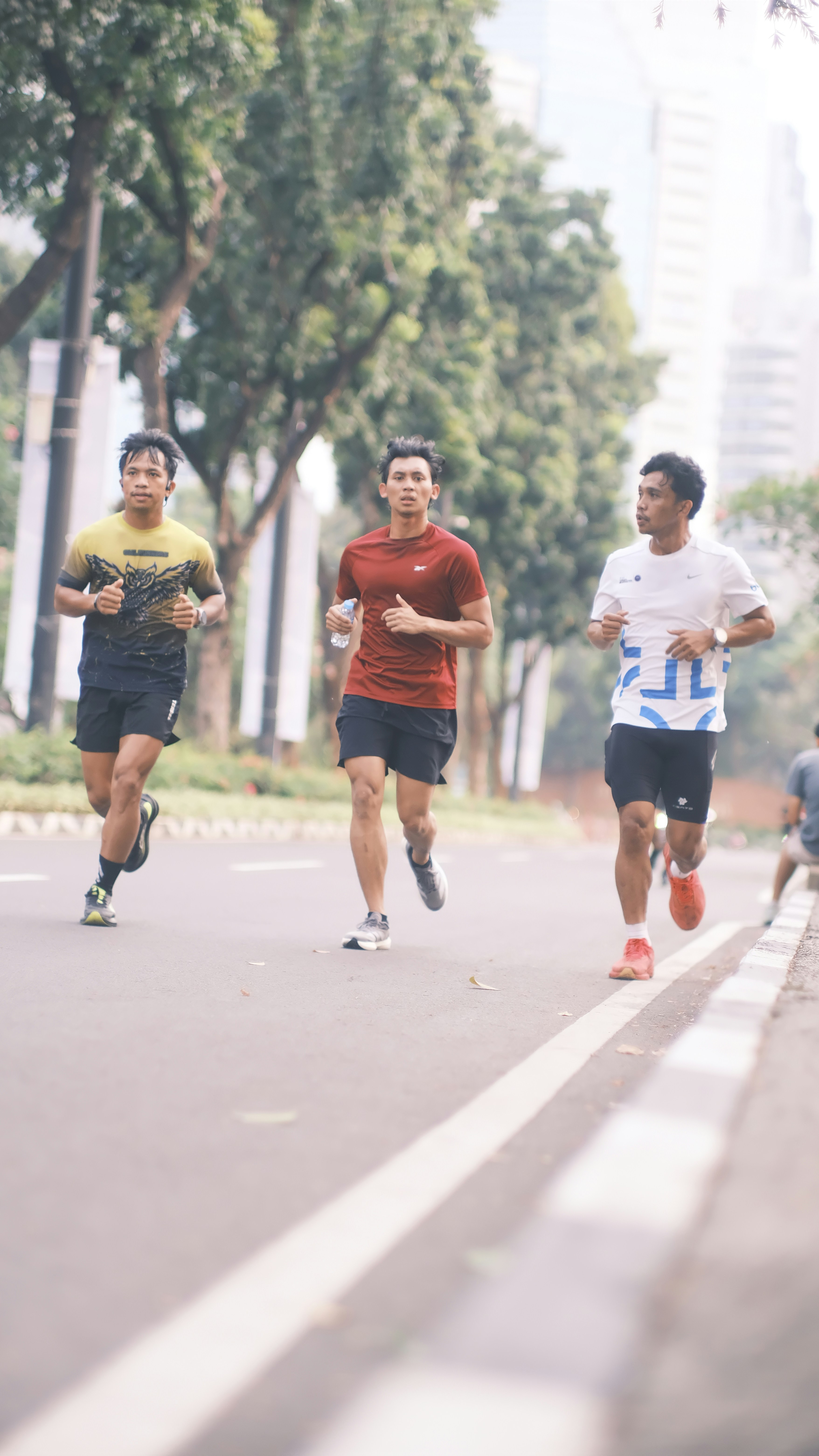 Three men running along a tree-lined city road during a morning workout