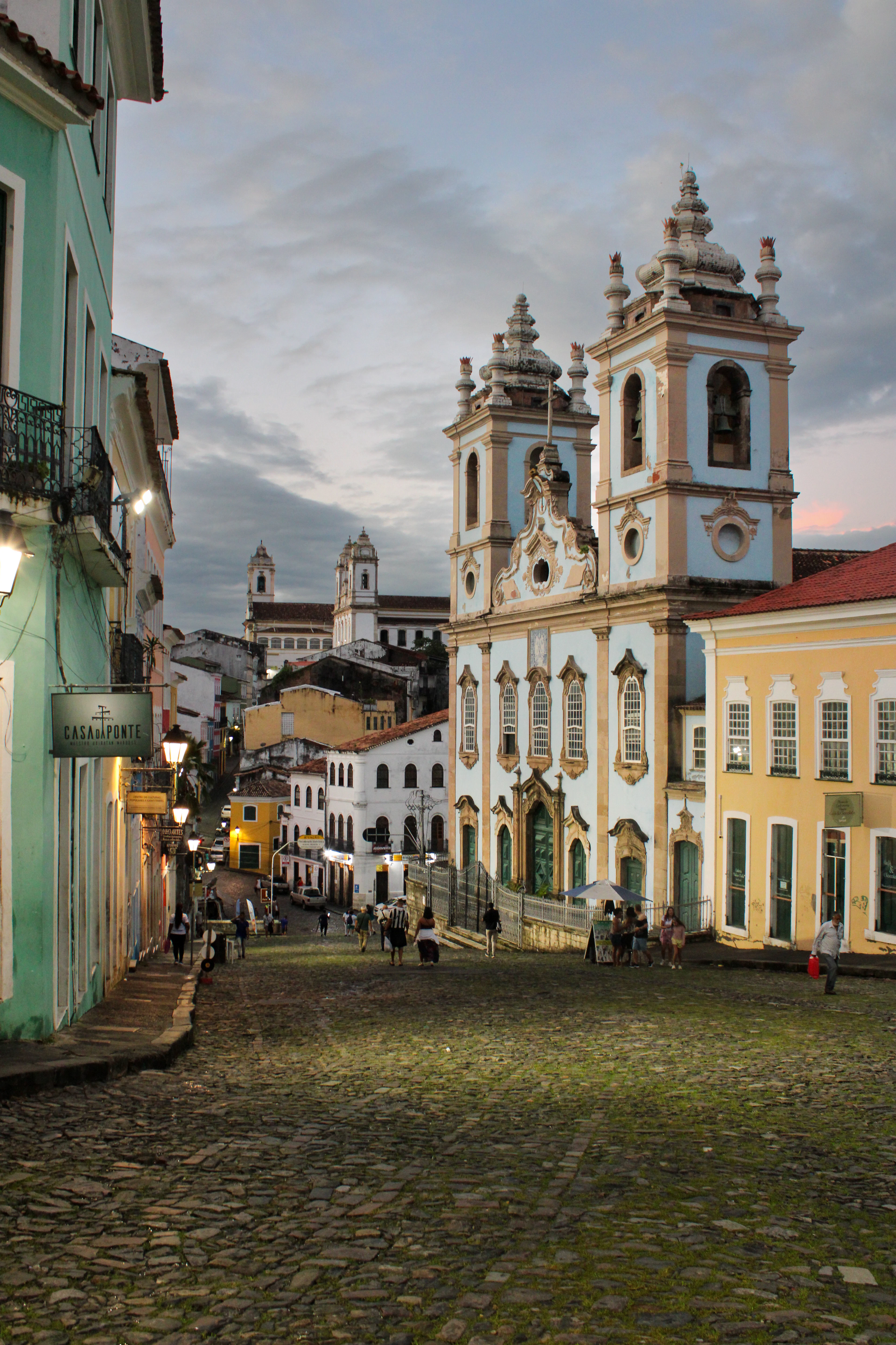 A cobbled street leading to a blue baroque church at dusk, Salvador, Brazil