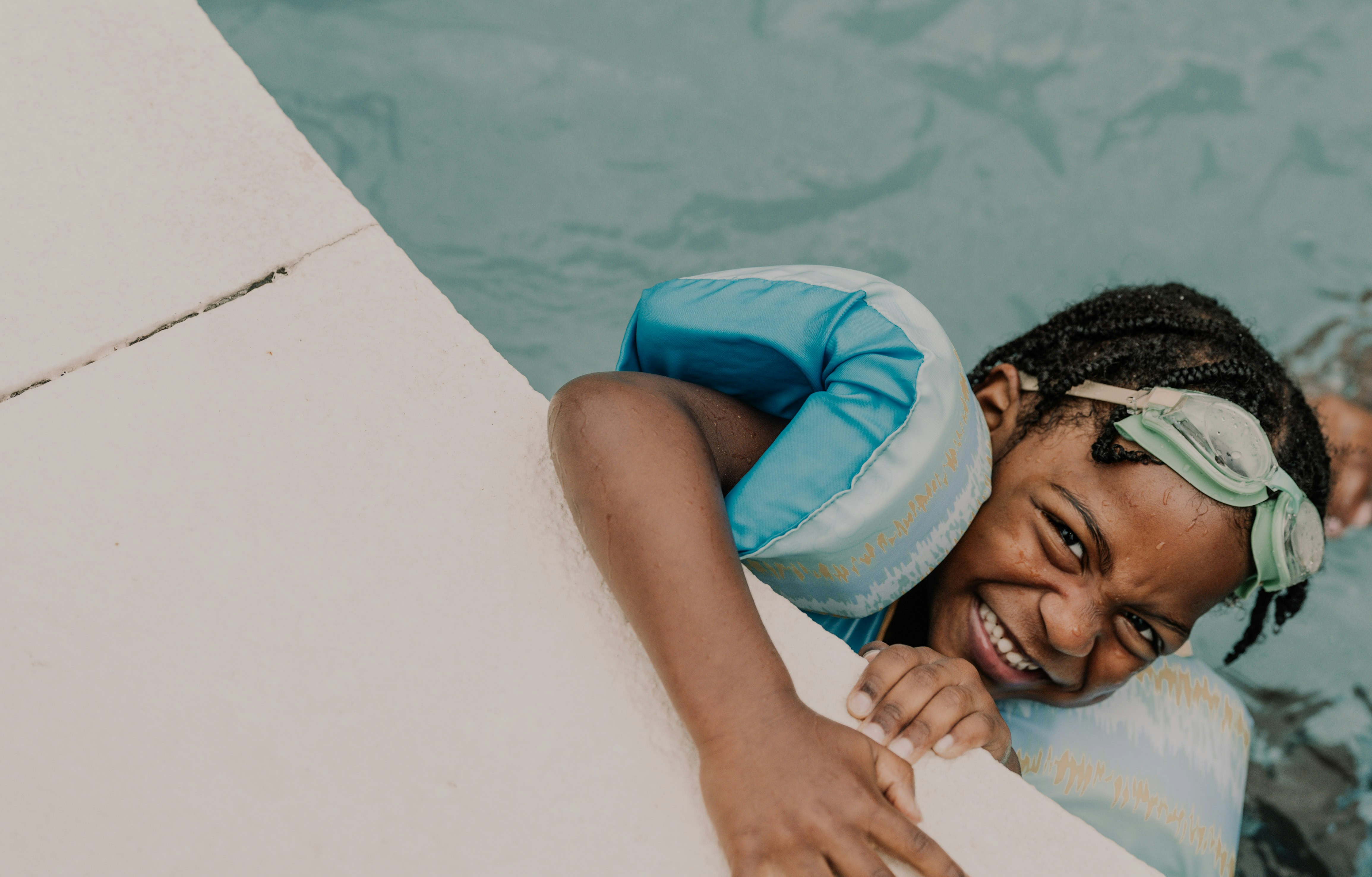 A smiling child wearing blue arm floaties and goggles in a swimming pool