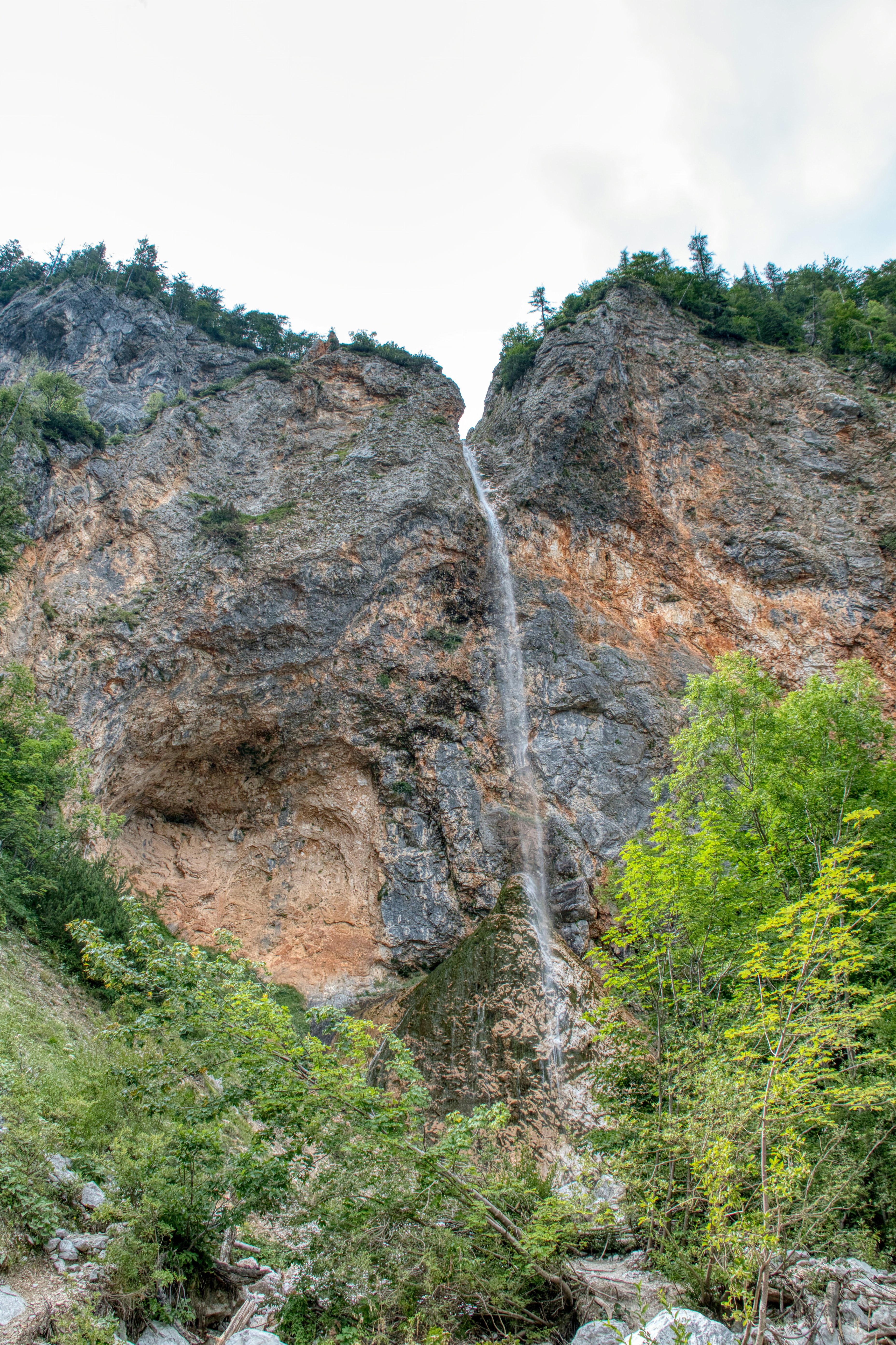 A thin waterfall cascading down a steep rocky cliff face with green trees
