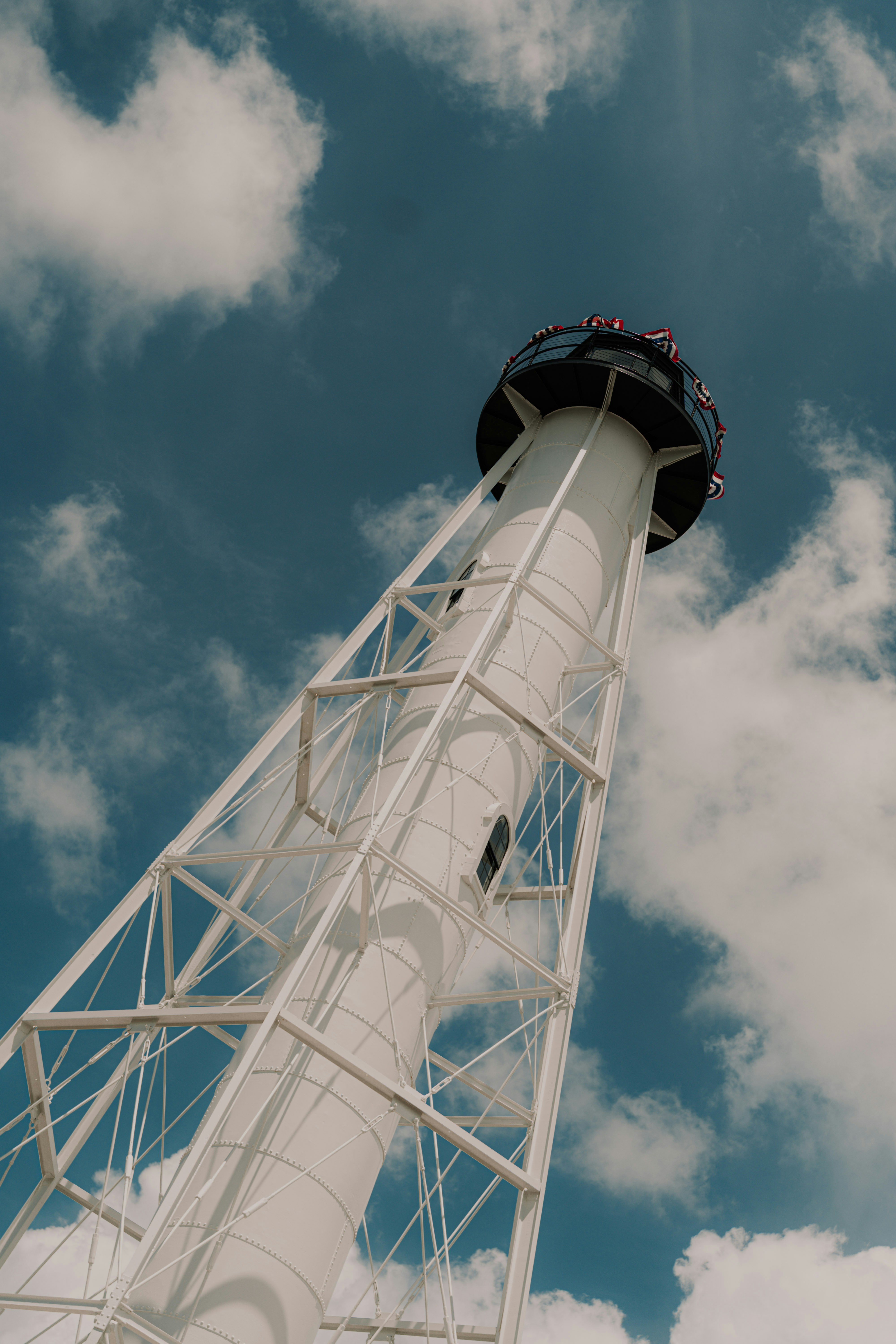 A white metal lighthouse tower against a blue sky with scattered white clouds