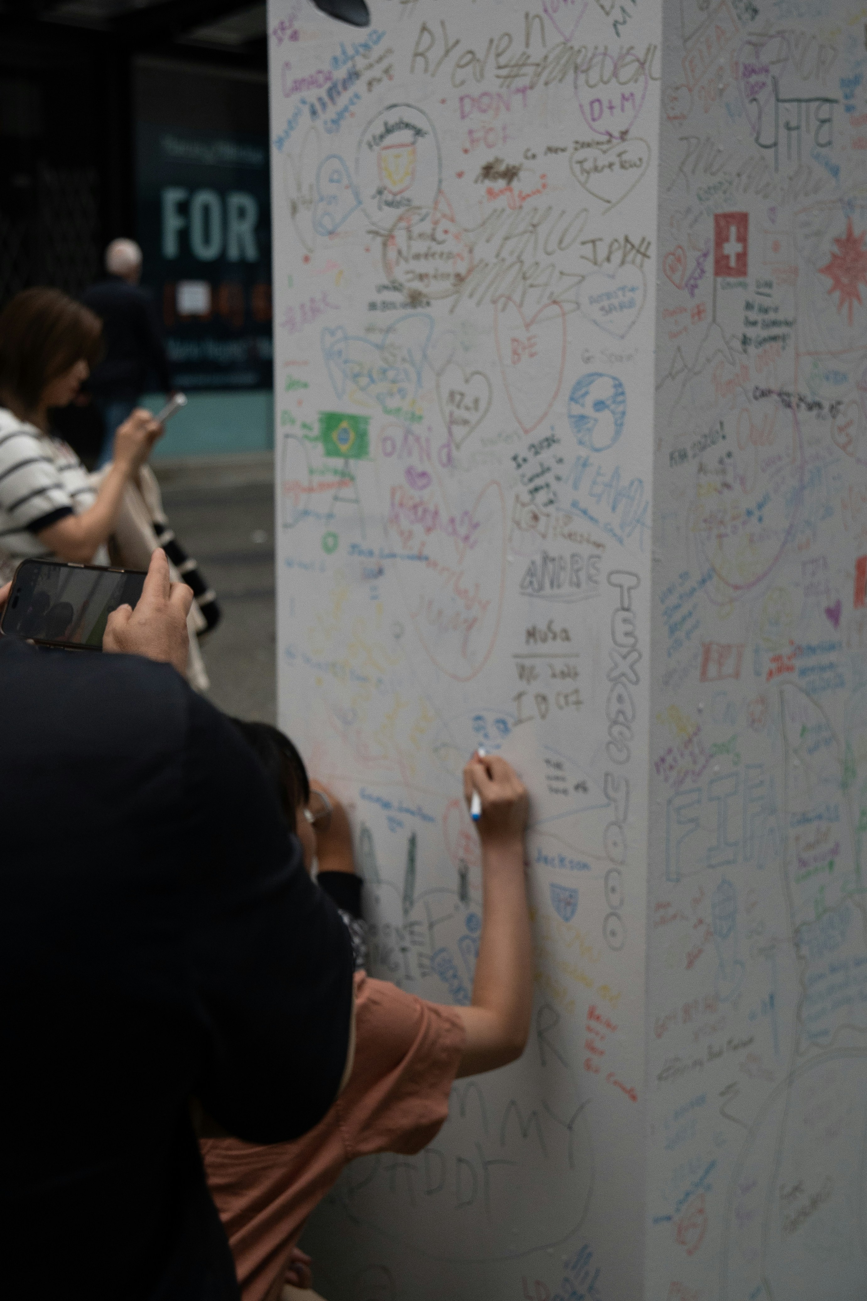 A person writing on a white pillar covered in colorful graffiti and signatures