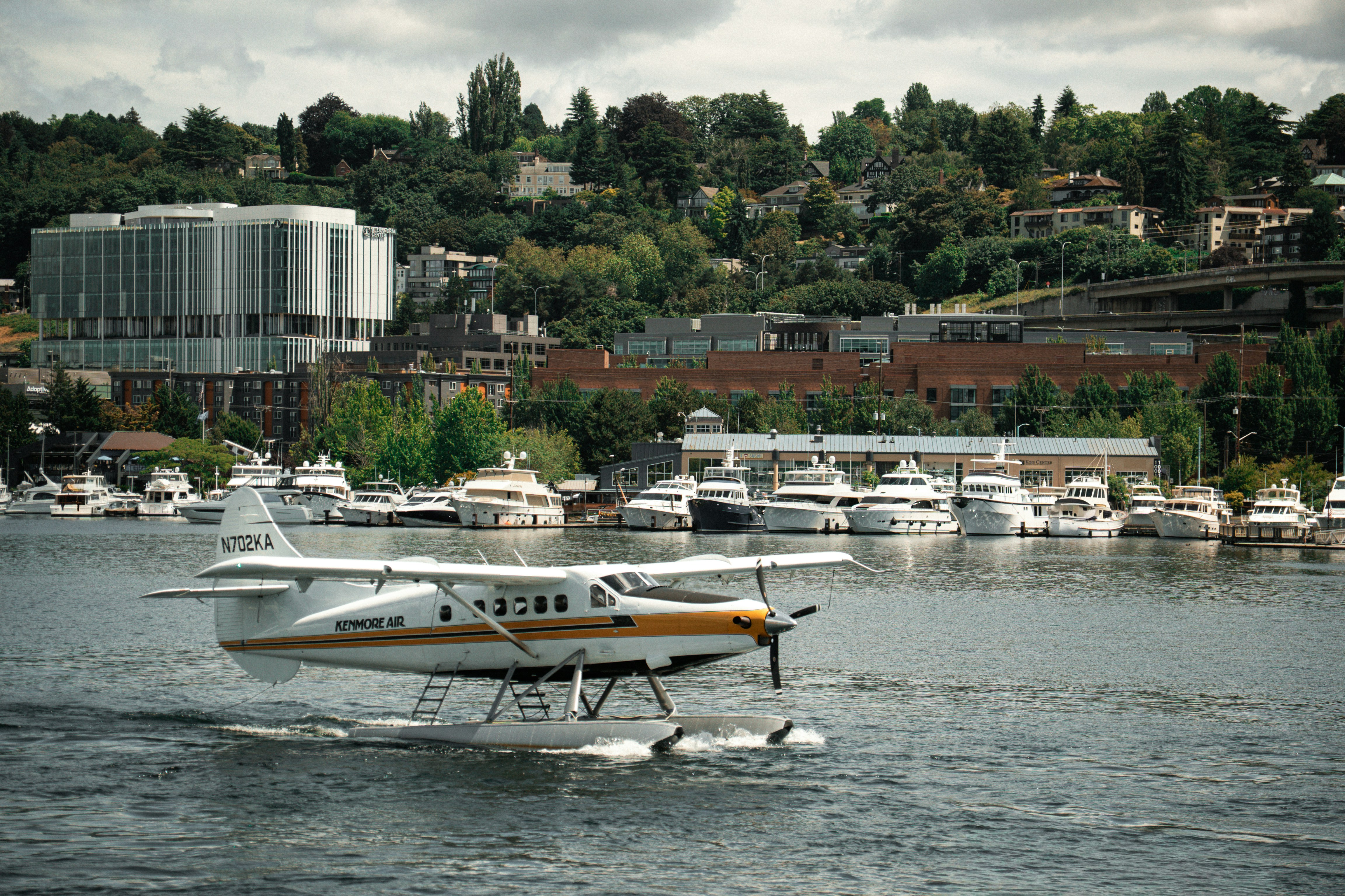 A white and yellow seaplane taxiing on Lake Union in Seattle with yachts