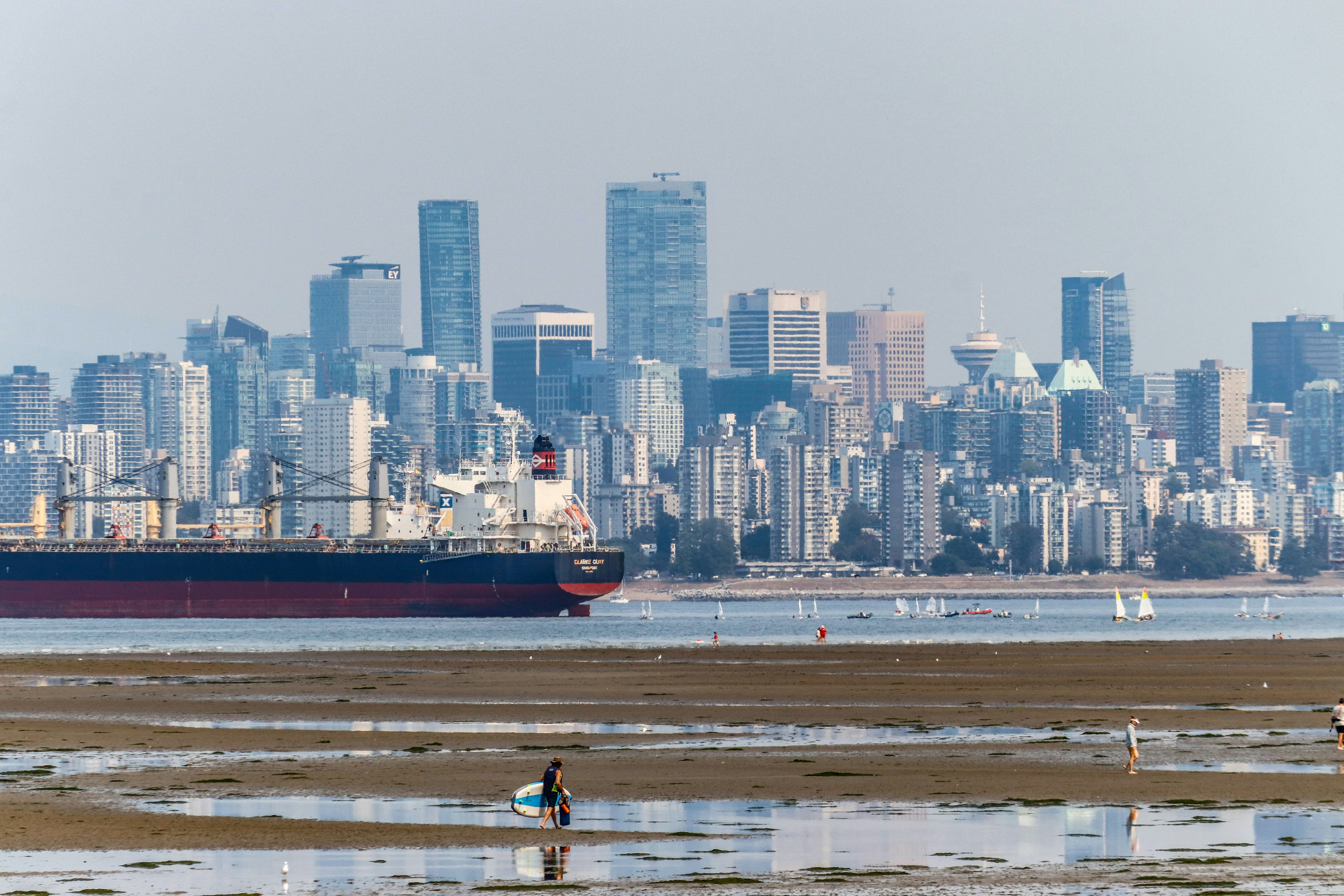 A large cargo ship passing the Vancouver skyline viewed from a sandy beach