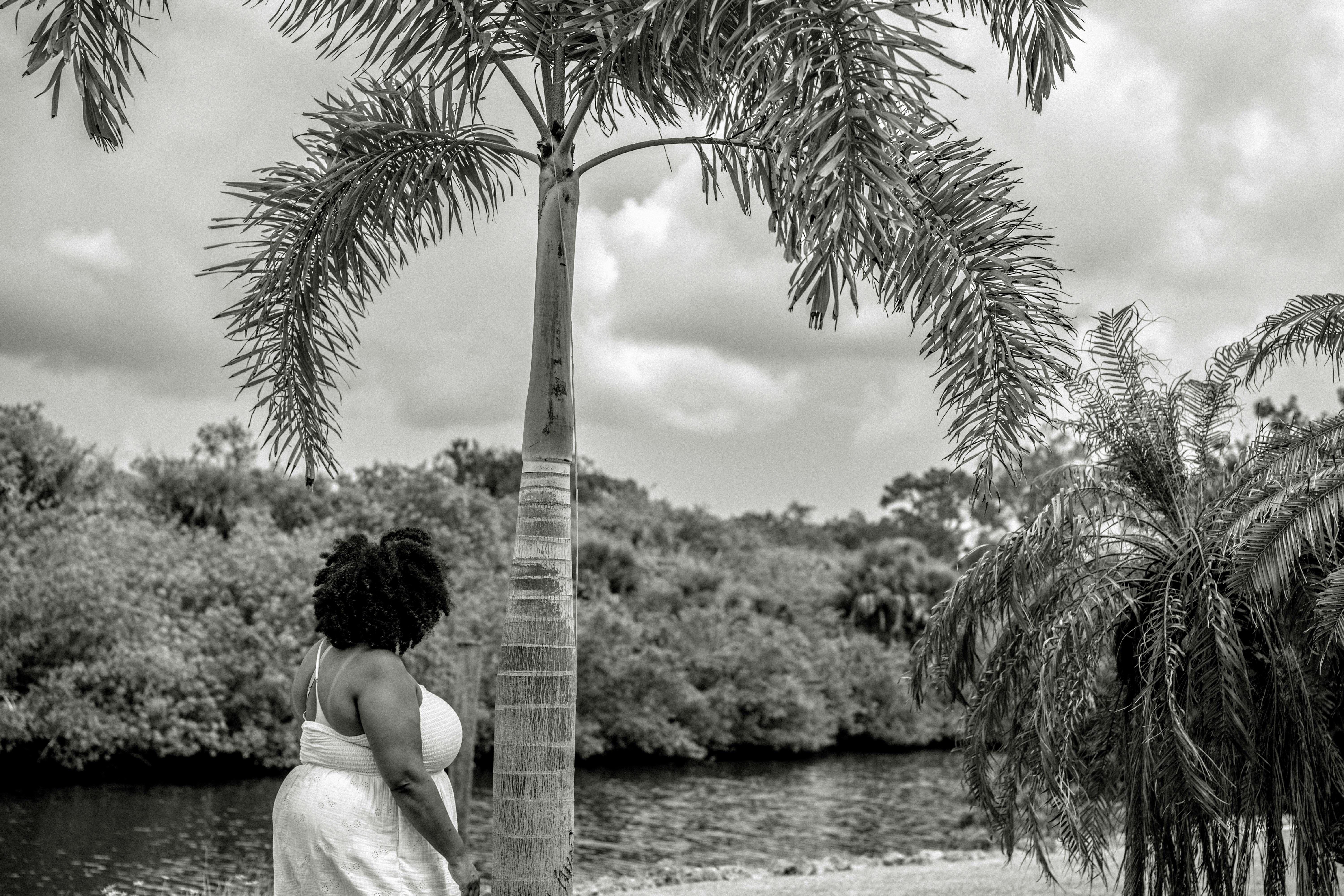 A woman in a white dress standing by a palm tree near water