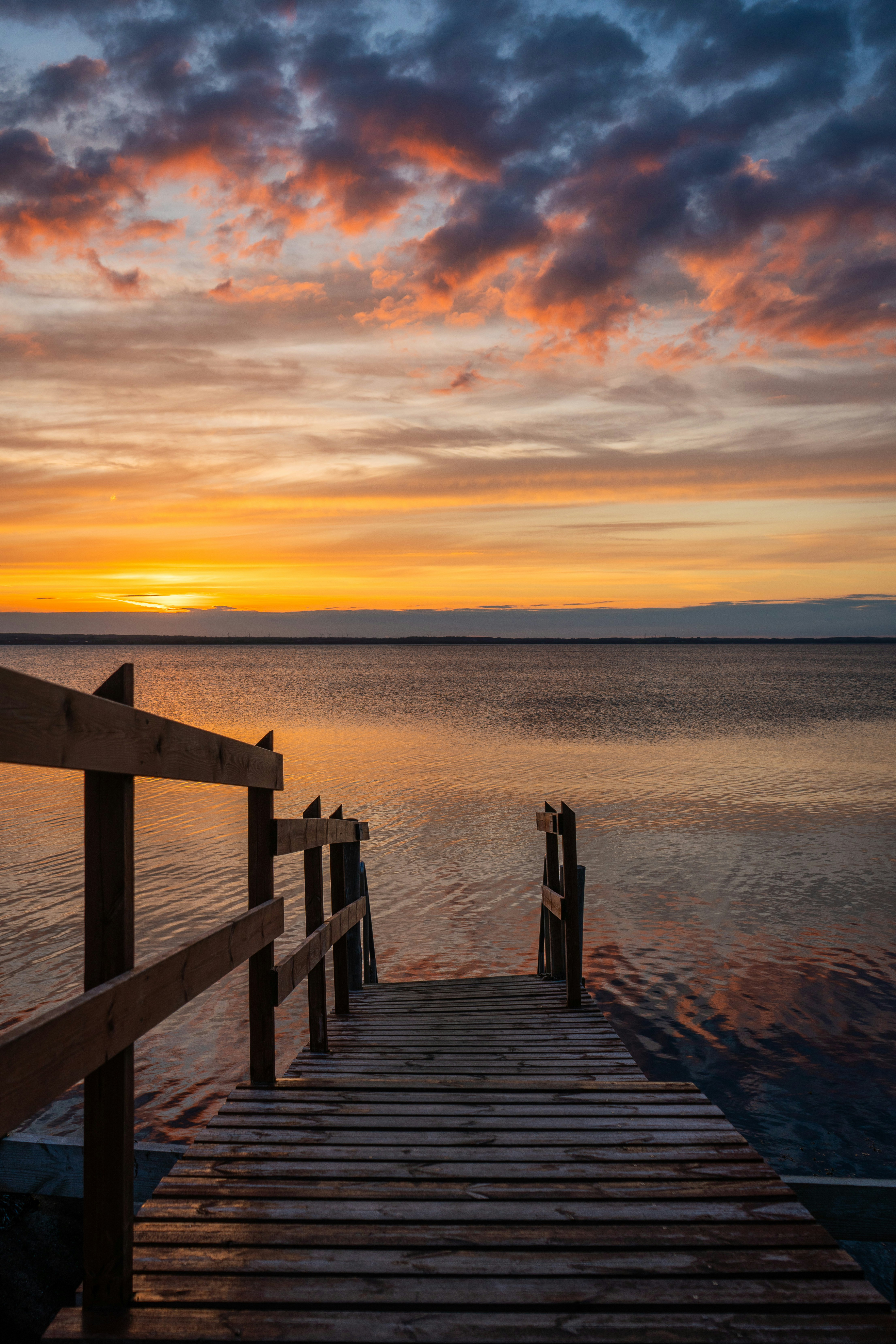 A wooden pier extending into calm water under a vibrant orange sky