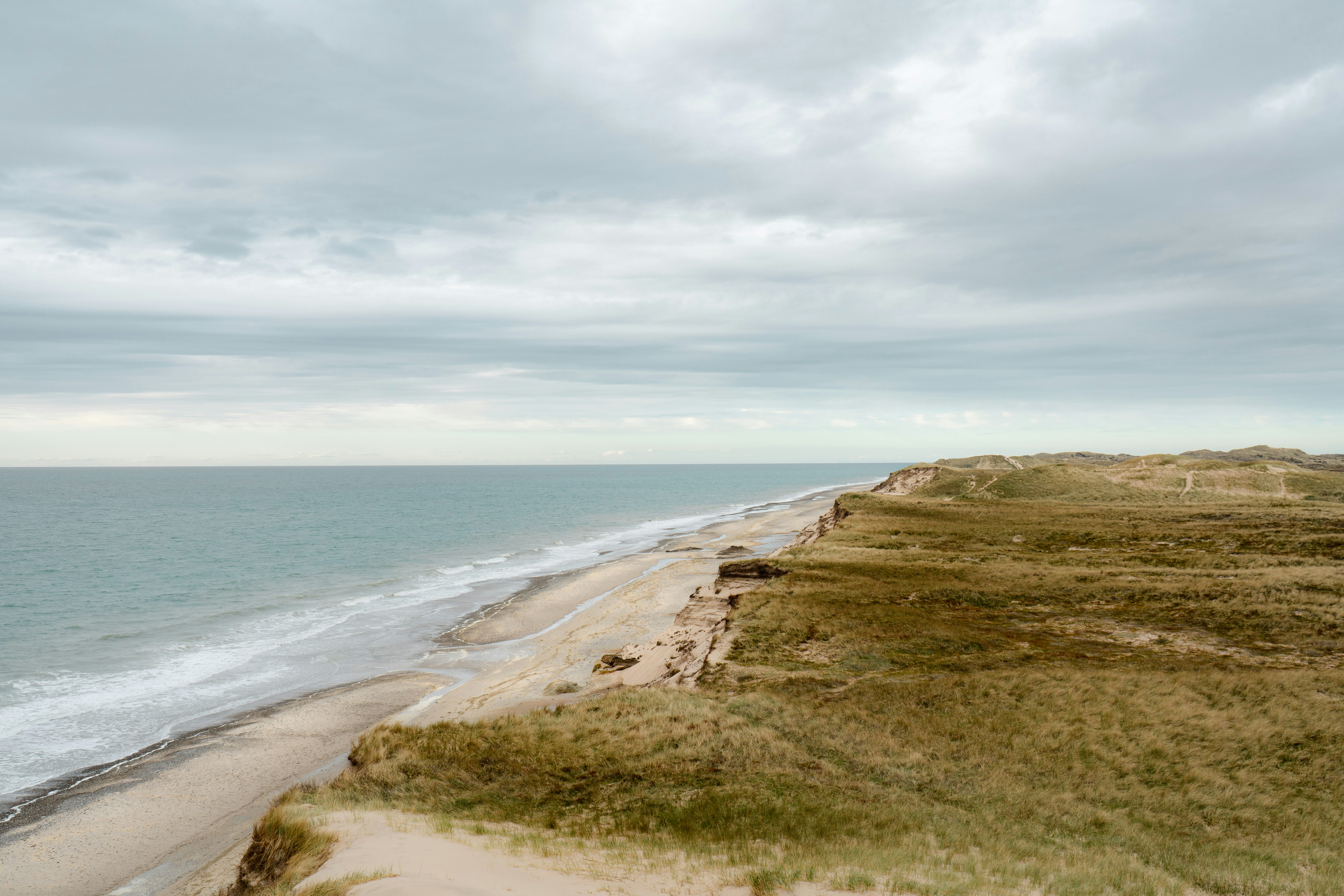 A sandy beach below grassy dunes under a vast overcast sky