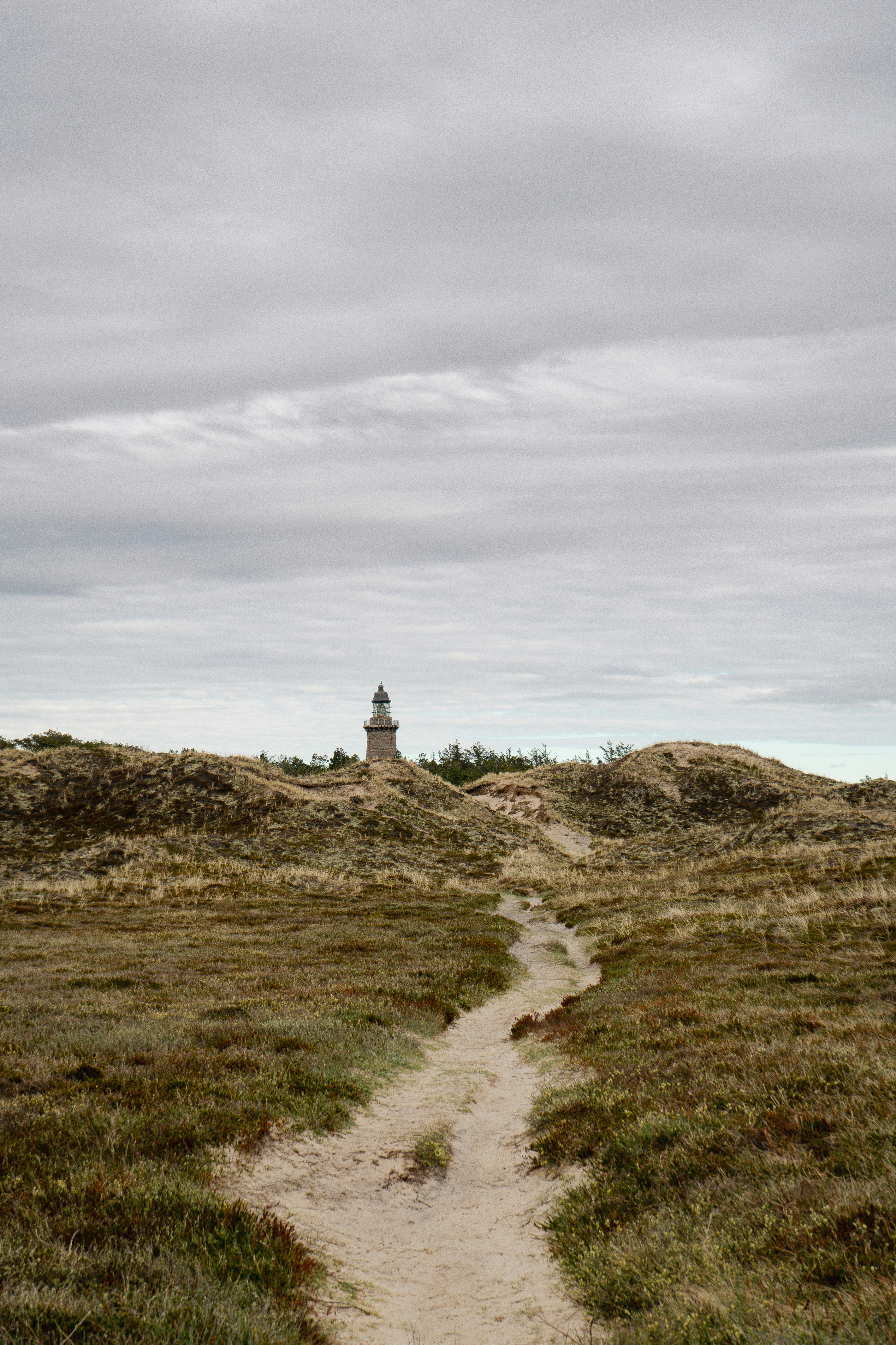 A lighthouse behind grassy sand dunes under a cloudy sky